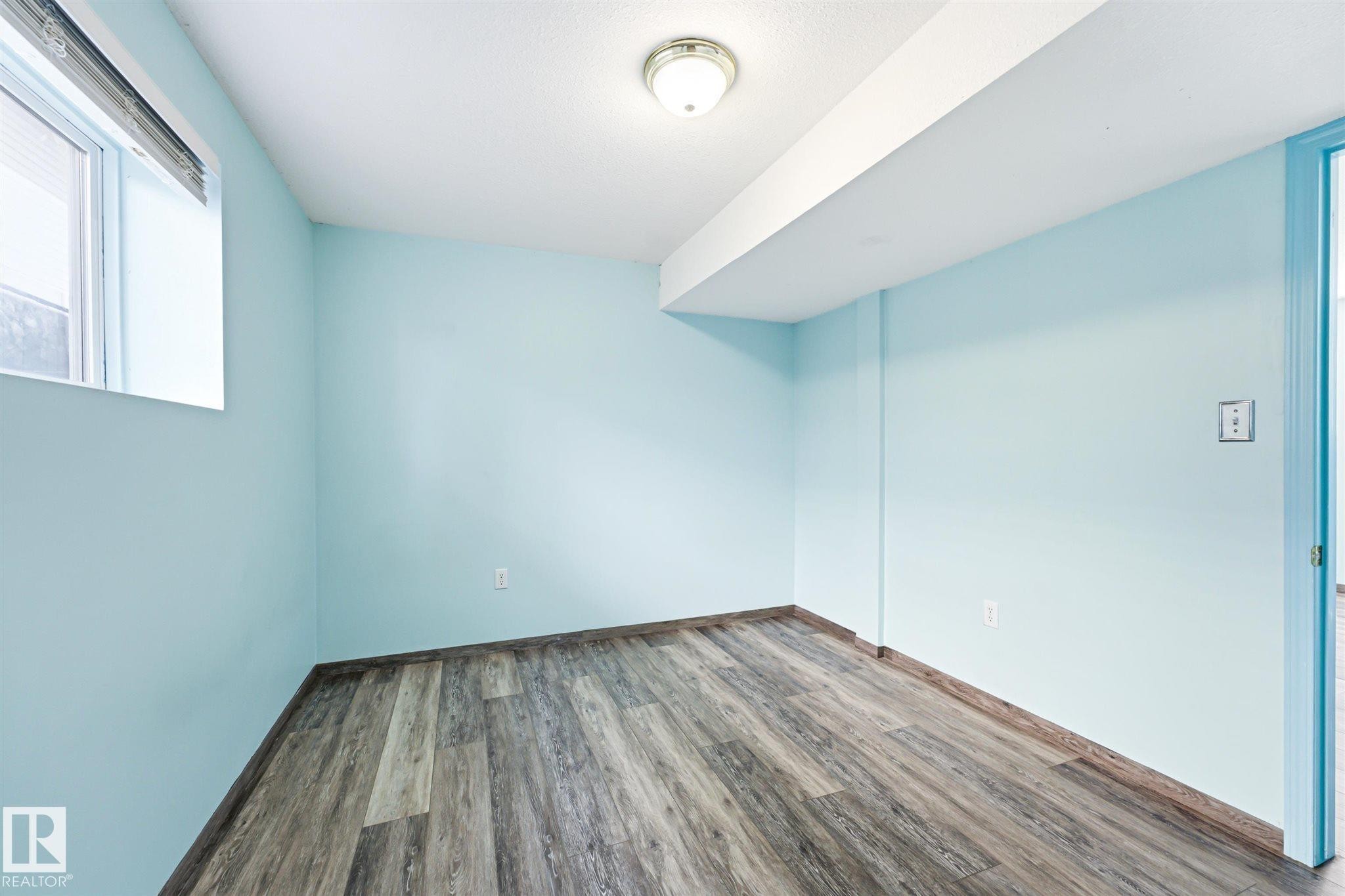 Room featuring light blue painted walls, wood-finish flooring, a window with blinds, and a flush mount ceiling light - 14908 137 Street Nw, Edmonton, AB - Indoor Photo Showing Other Room