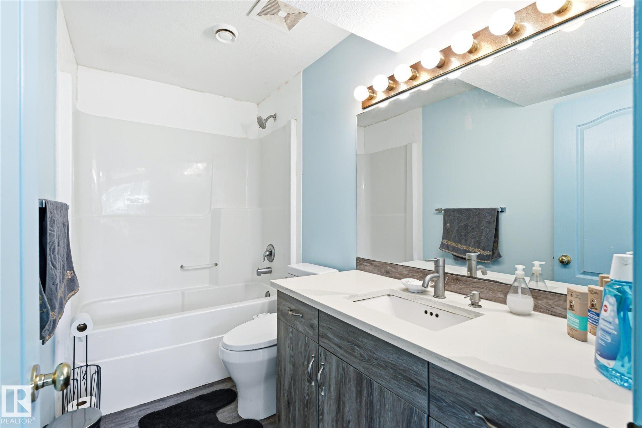Bathroom featuring a white tub-shower combination, a vanity with wood-finish cabinetry, a white countertop, and a large mirror - 14908 137 Street Nw, Edmonton, AB - Indoor Photo Showing Bathroom