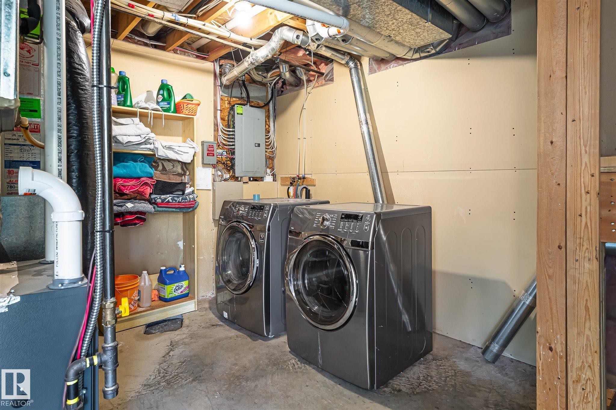 Utility area featuring concrete flooring, exposed ceiling joists and ductwork, a built-in shelving unit, and painted wall panels - 14908 137 Street Nw, Edmonton, AB - Indoor Photo Showing Laundry Room