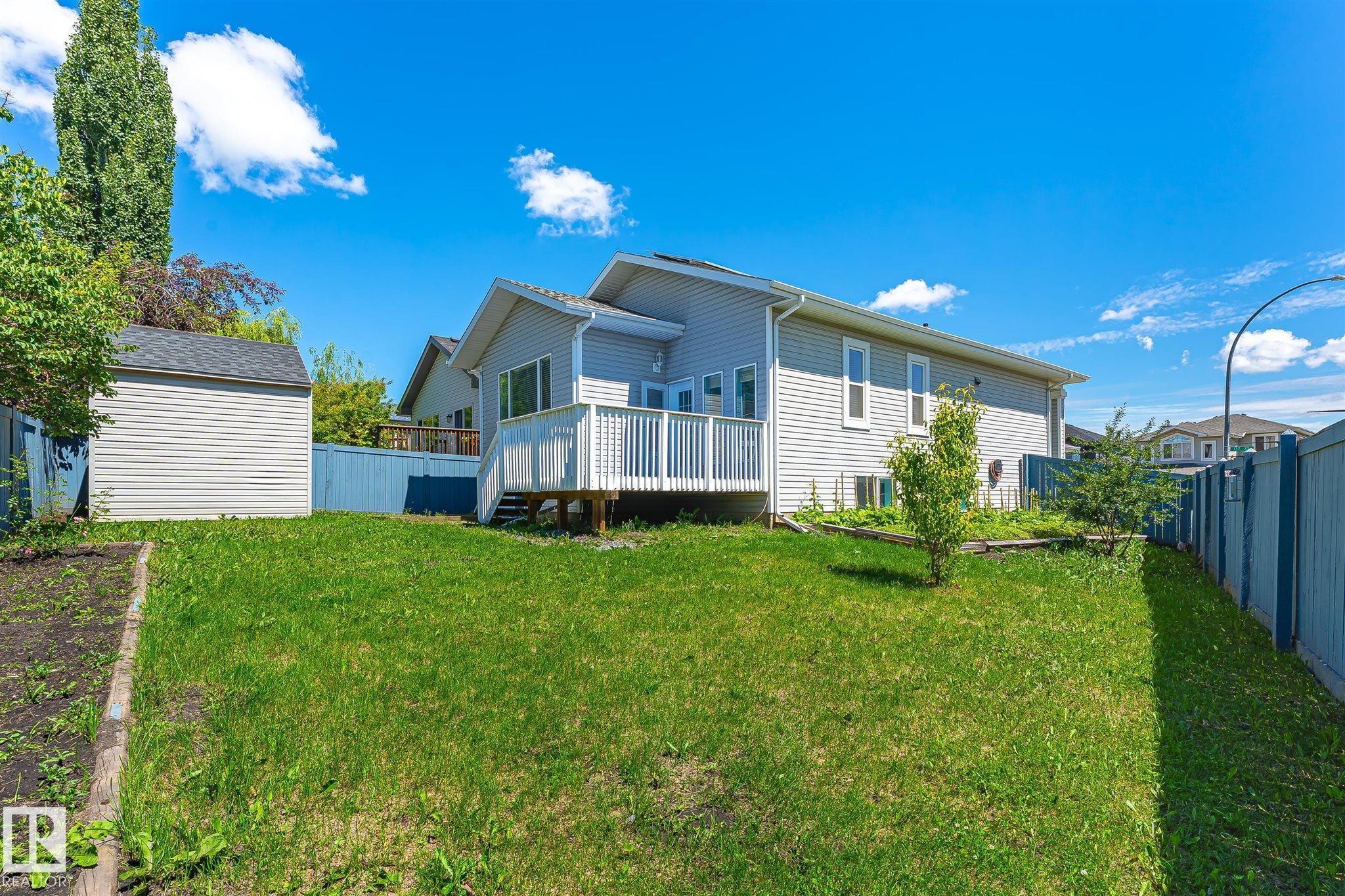 Spacious backyard featuring a manicured lawn, an elevated deck with white railings, a separate storage shed, and a fenced perimeter - 14908 137 Street Nw, Edmonton, AB - Outdoor