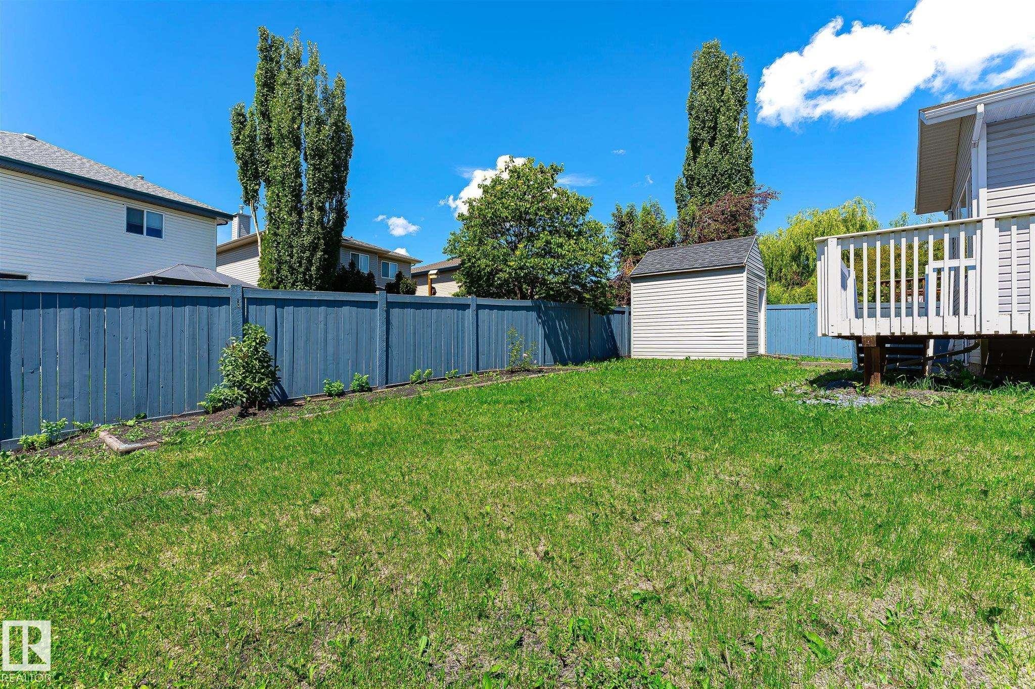 Fenced backyard featuring a storage shed, a raised deck with white railings, and a planting bed along the perimeter - 14908 137 Street Nw, Edmonton, AB - Outdoor