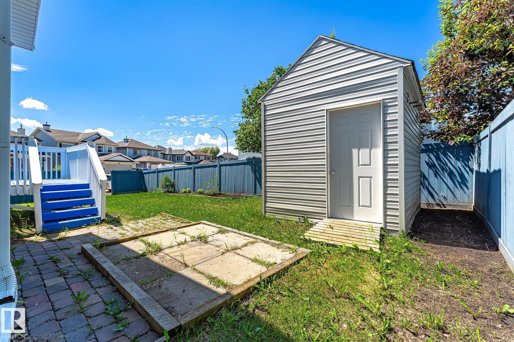 Backyard featuring a detached storage shed, a paved patio area, and a wooden deck with painted stairs - 14908 137 Street Nw, Edmonton, AB - Outdoor
