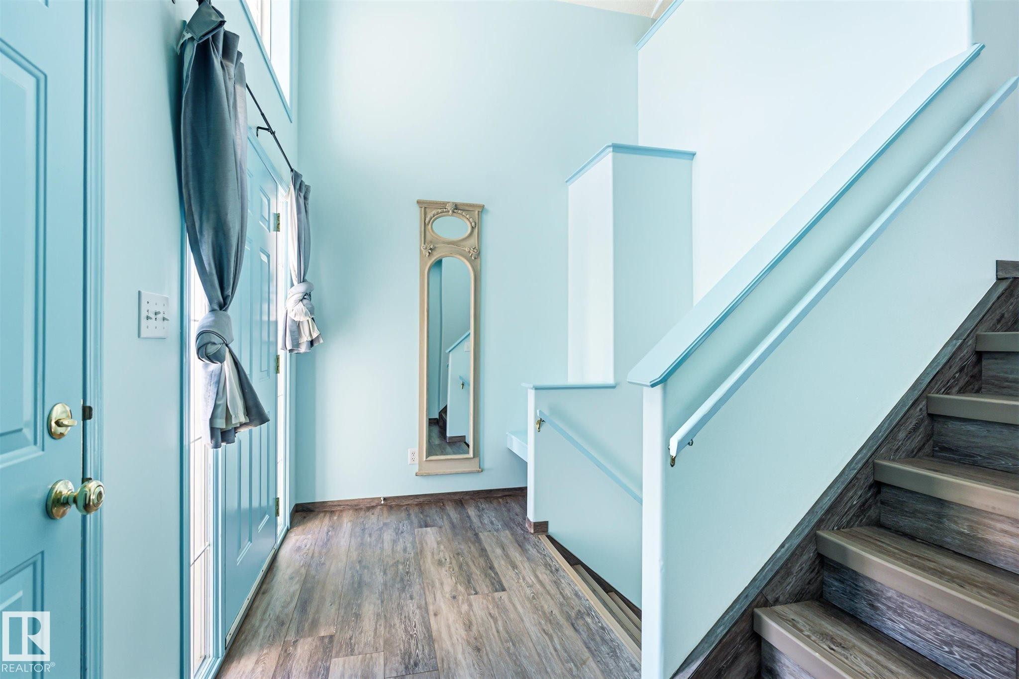 Entryway featuring wood-finish flooring, a light-colored painted interior door, light blue wall paint, and a staircase with wood-finish treads and risers - 14908 137 Street Nw, Edmonton, AB - Indoor Photo Showing Other Room