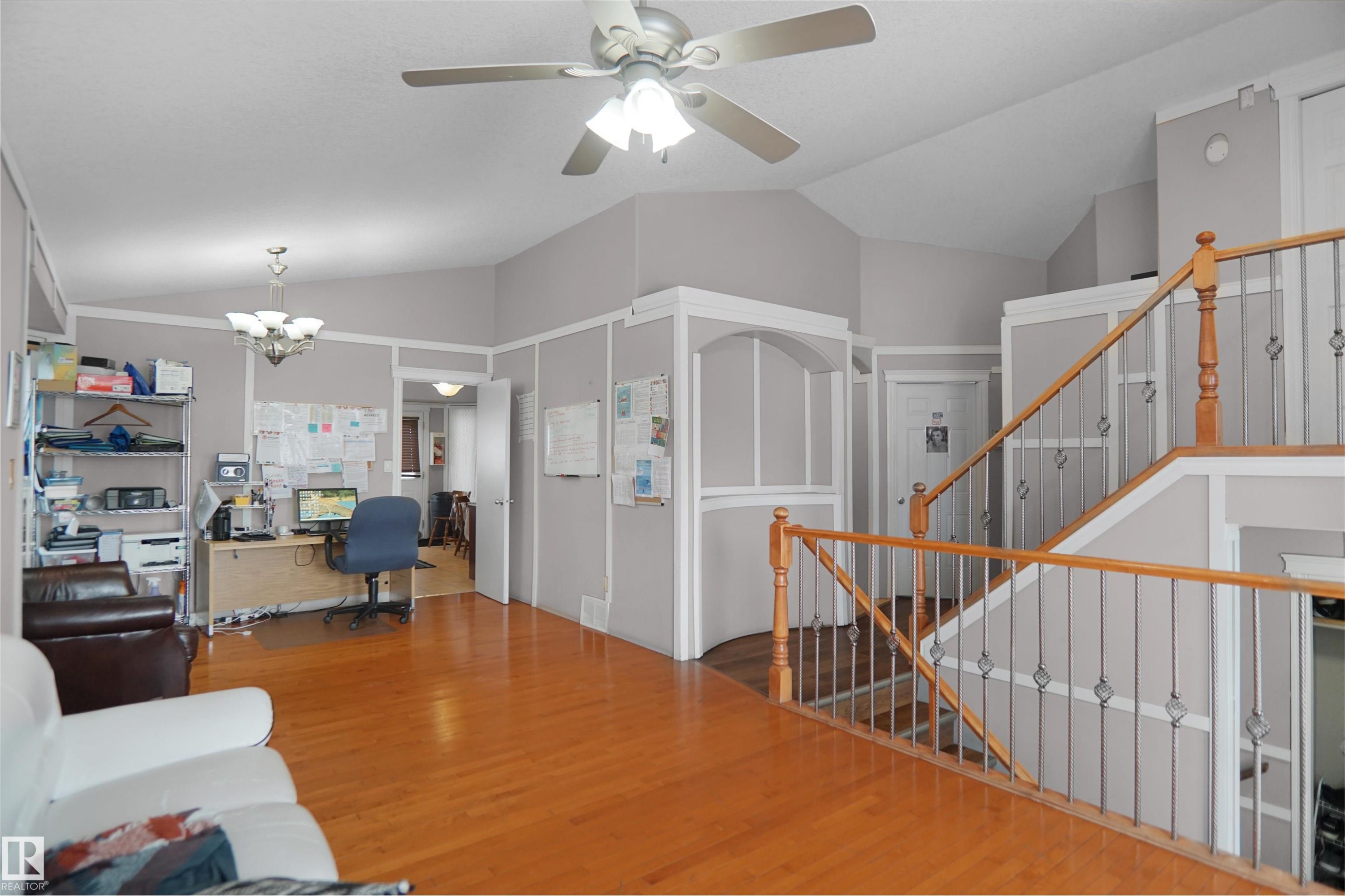 Open concept living area featuring wood-finish flooring, vaulted ceilings, a ceiling fan with integrated lighting, and a staircase with wood railing and iron balusters - 4816 155 Ave, Edmonton, AB