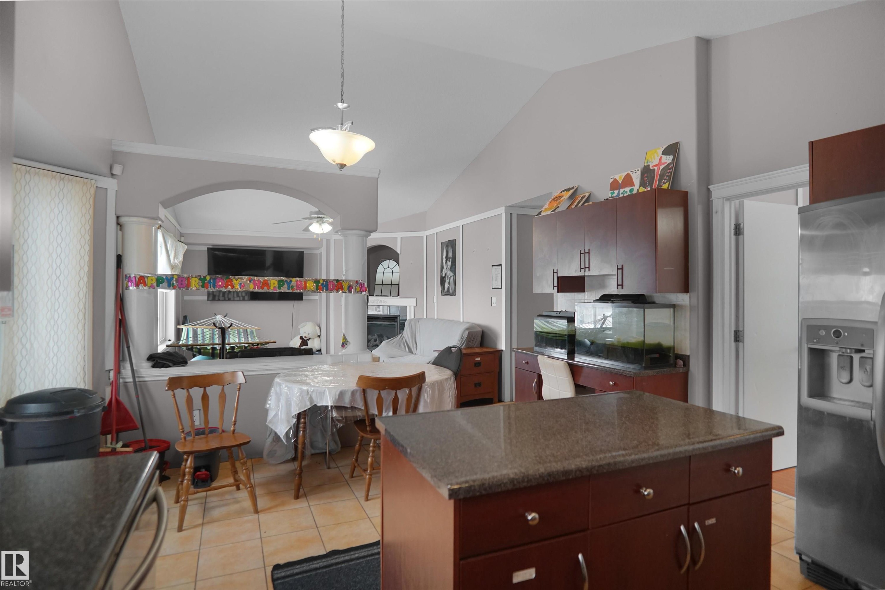 Kitchen featuring a central island with a granite-style countertop, mahogany-finish cabinetry, and ceramic tile flooring - 4816 155 Ave, Edmonton, AB