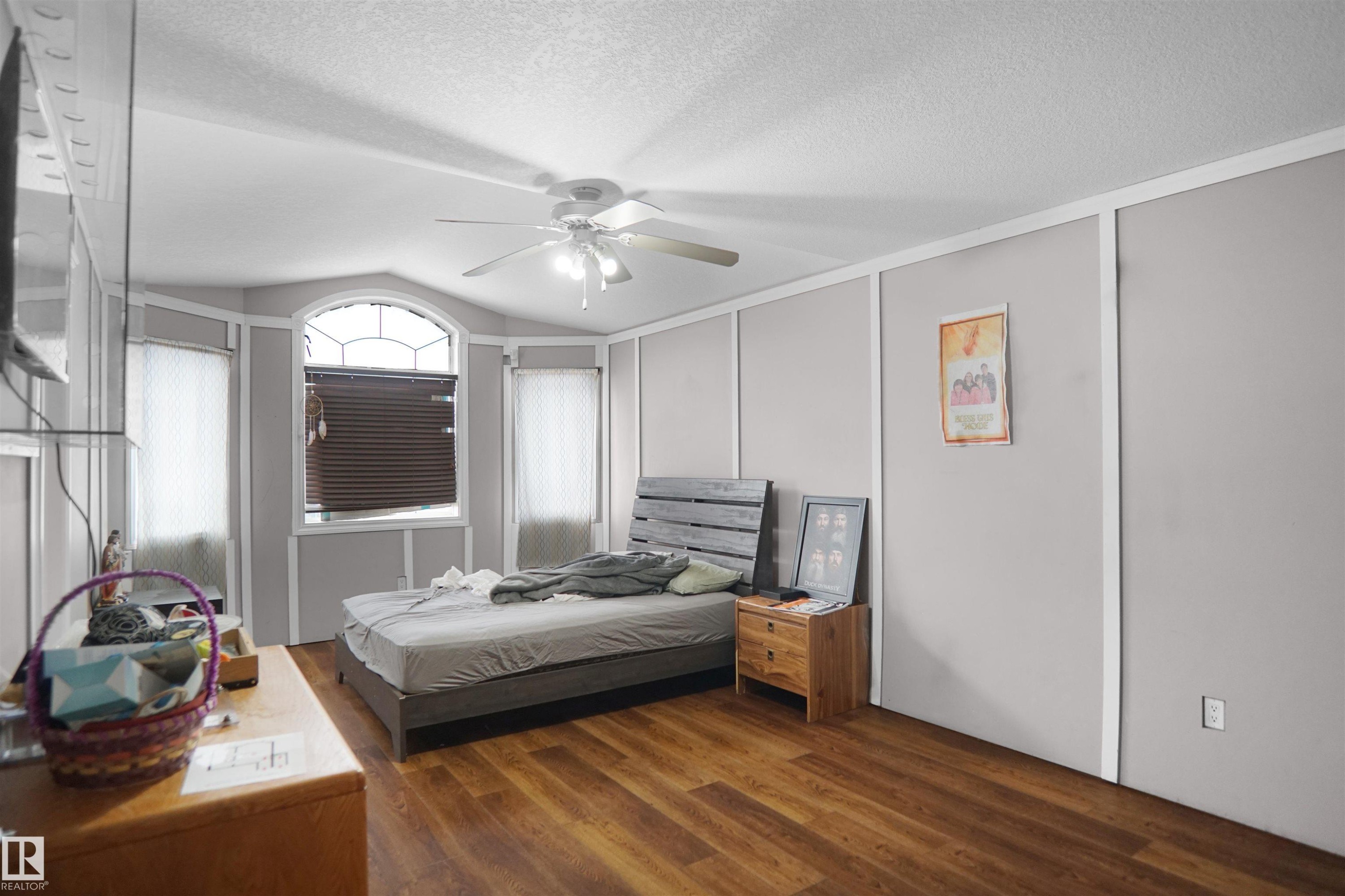 Room featuring wood-finish flooring, a ceiling fan with integrated lighting, and multiple windows - 4816 155 Ave, Edmonton, AB