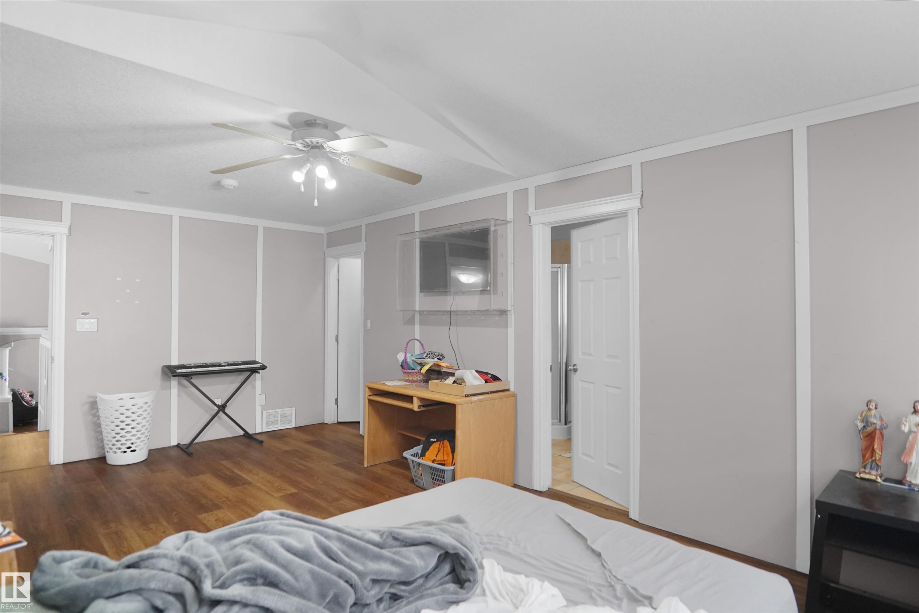 Spacious room with wood-finish flooring, ceiling fan, and light gray paneled walls with white trim - 4816 155 Ave, Edmonton, AB