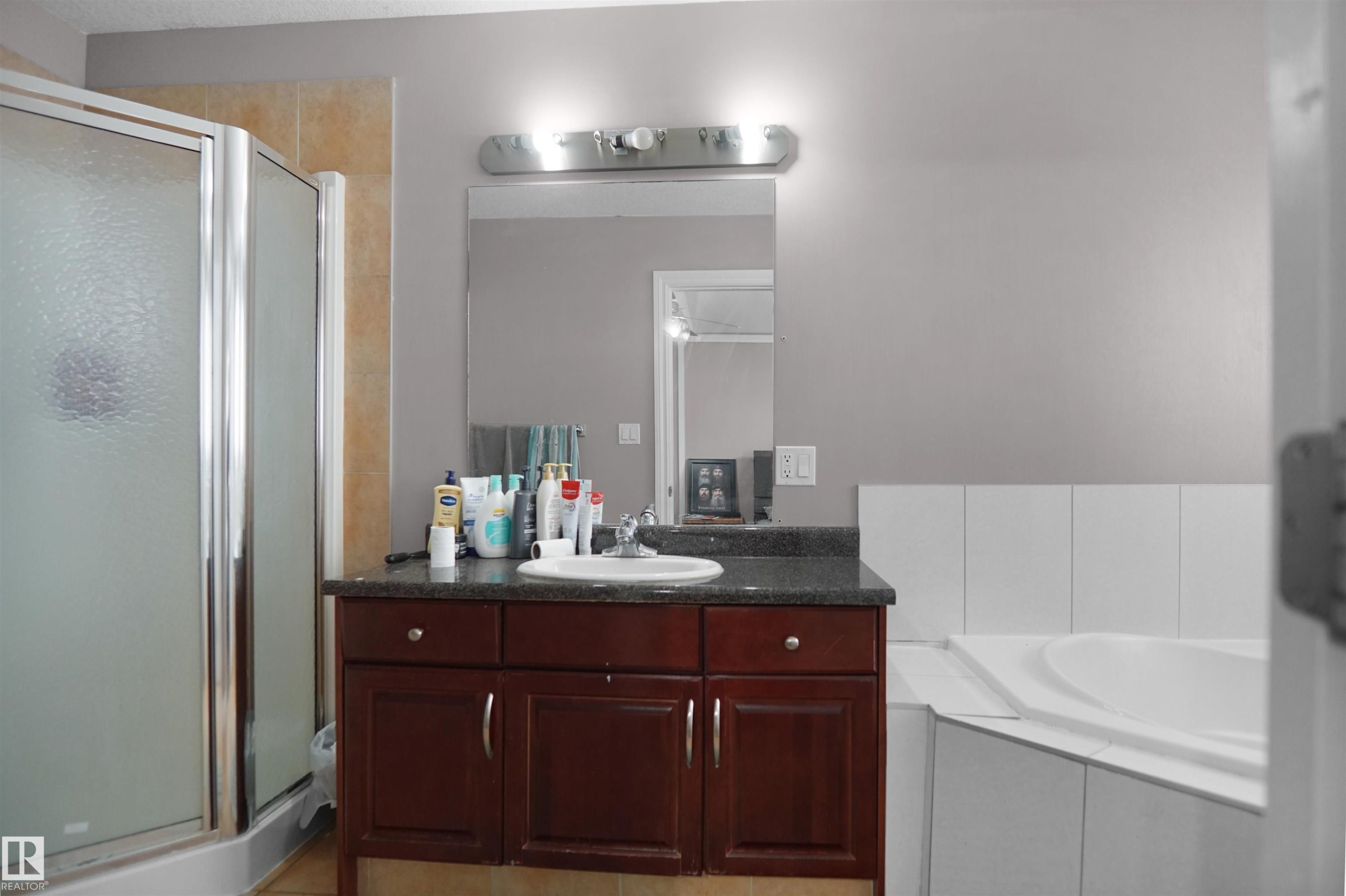 Bathroom featuring a glass-enclosed shower, a built-in corner bathtub, and a vanity with a dark countertop and wood-finish cabinetry - 4816 155 Ave, Edmonton, AB