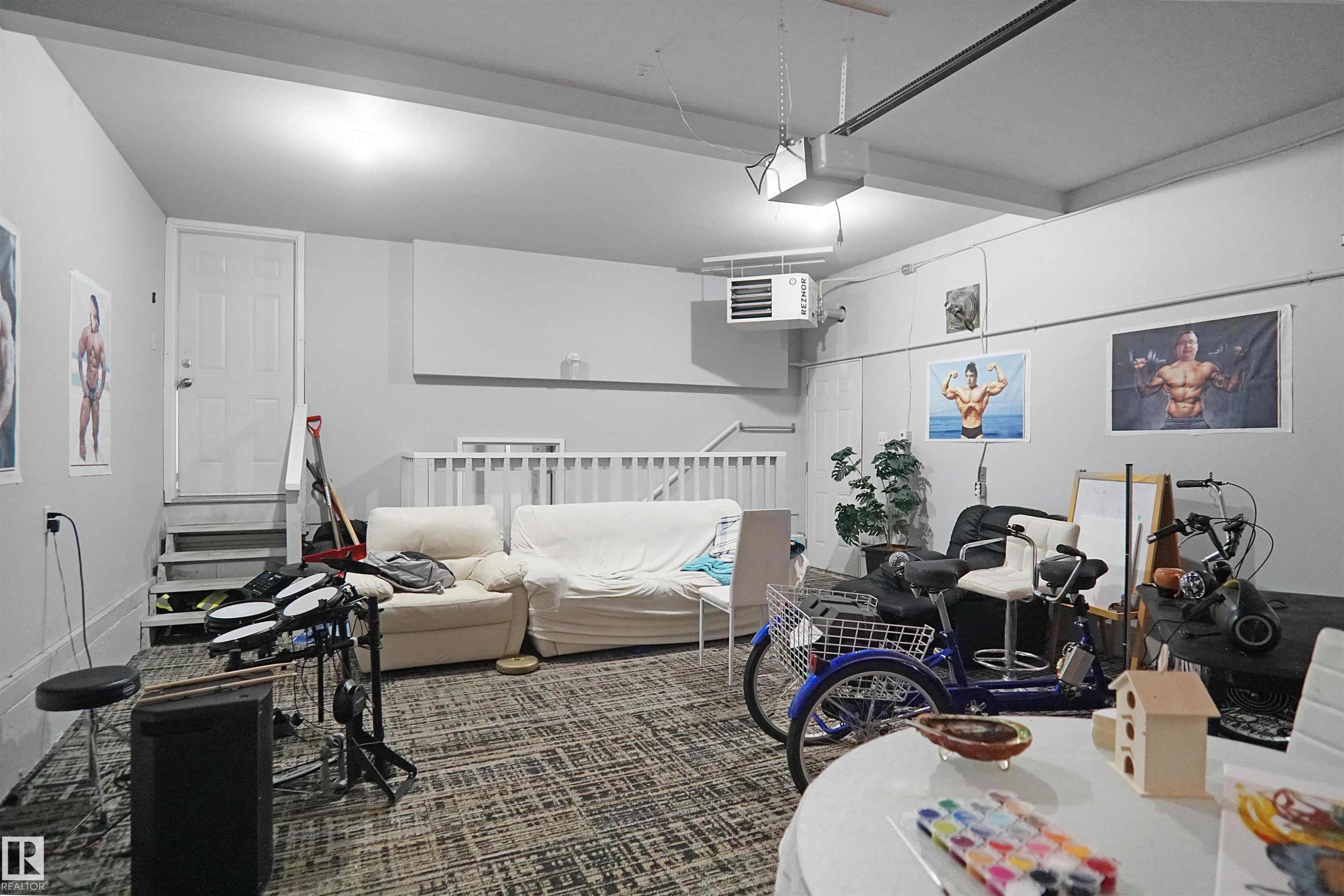 Spacious garage featuring light gray walls, textured carpeting, overhead lighting, and a white access door with stairs - 4816 155 Ave, Edmonton, AB