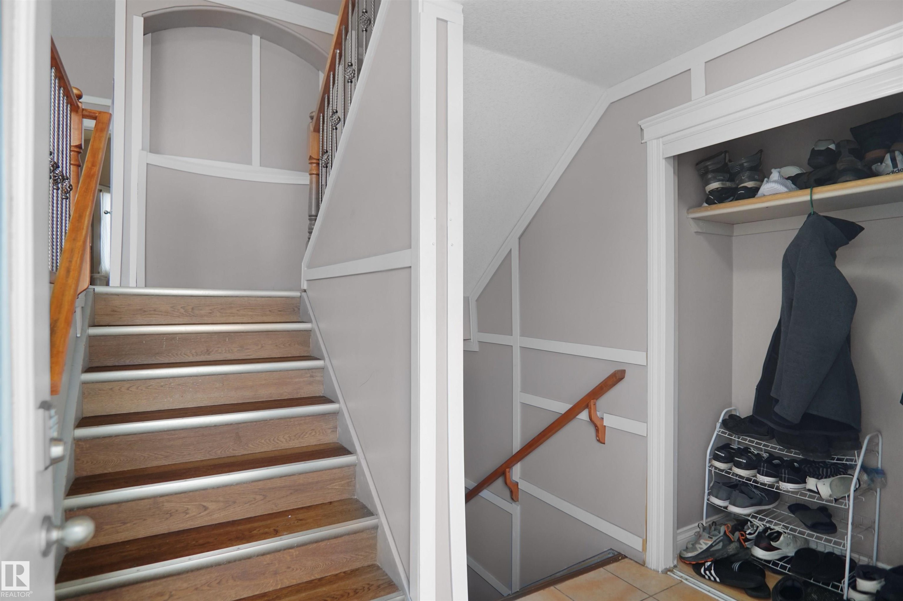 Split-level entry featuring wood-finish flooring on stairs with non-slip treads, white wainscoting, and a built-in closet with shelving and hanging space - 4816 155 Ave, Edmonton, AB