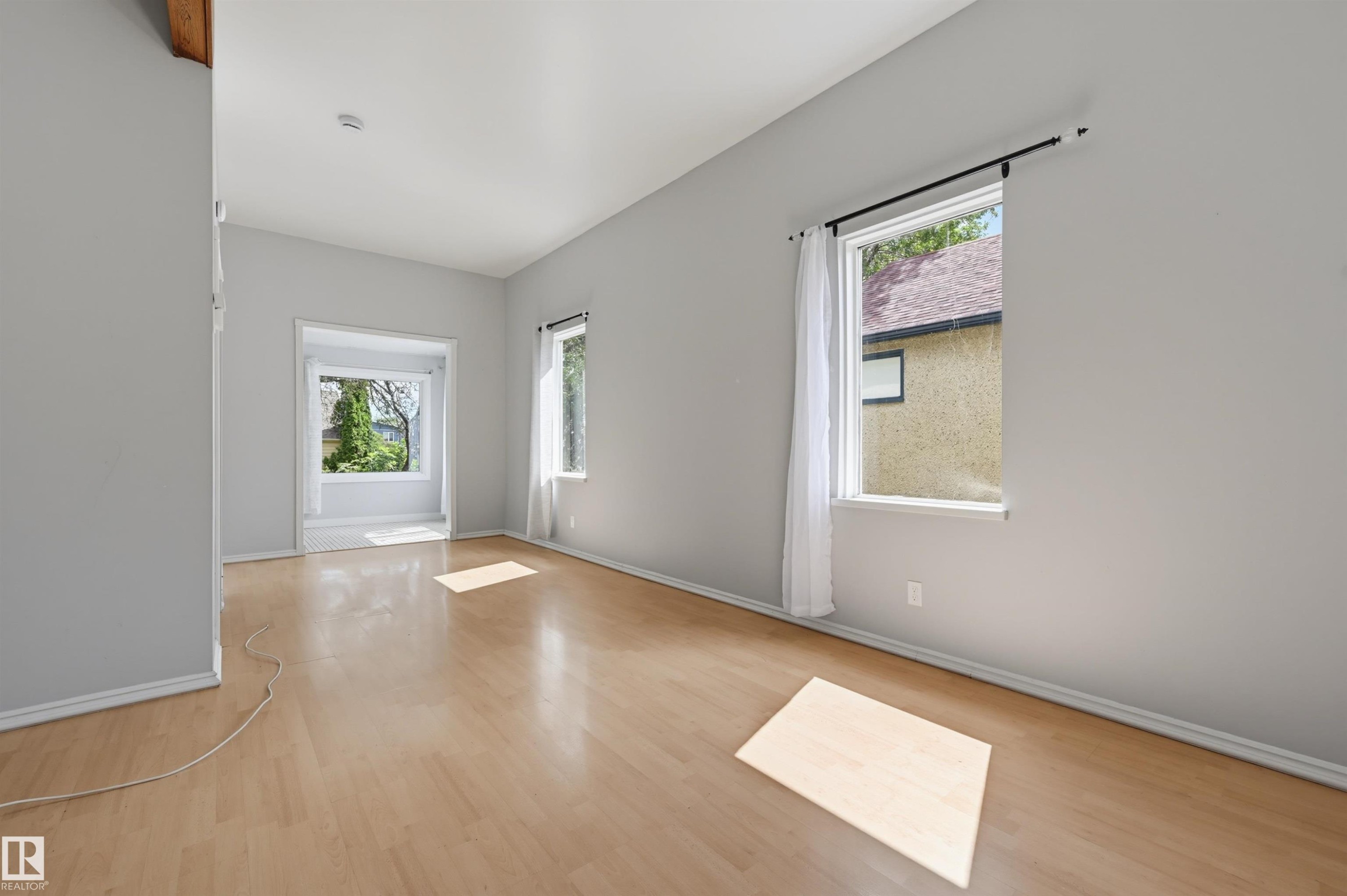 Spacious room featuring light wood-finish flooring, light grey painted walls, white baseboards, and multiple windows - 11450 71 Street Nw, Edmonton, AB