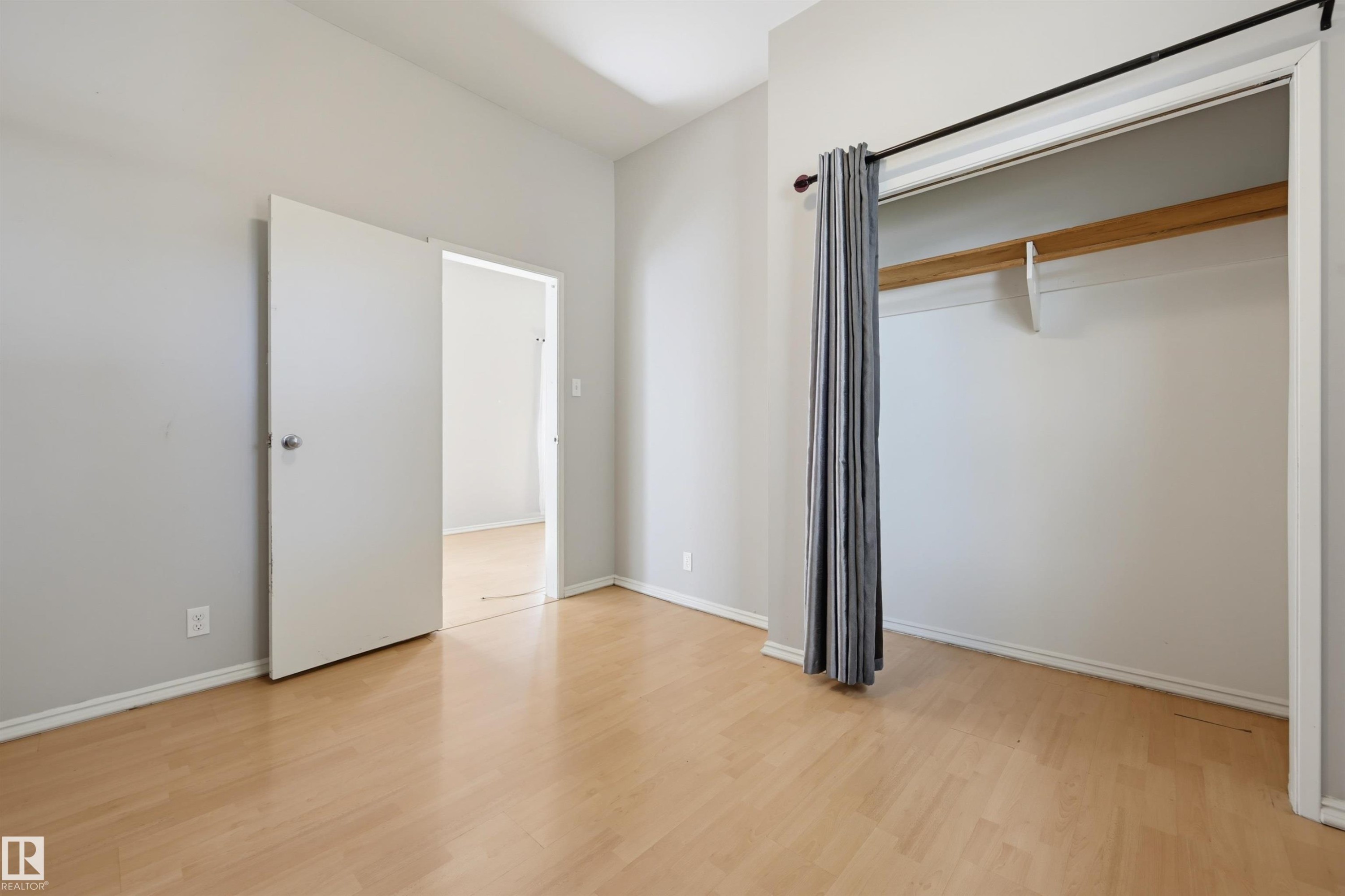 Bright room featuring wood-finish flooring, light gray wall paint, white trim, and a functional closet with a hanging rod and shelf - 11450 71 Street Nw, Edmonton, AB
