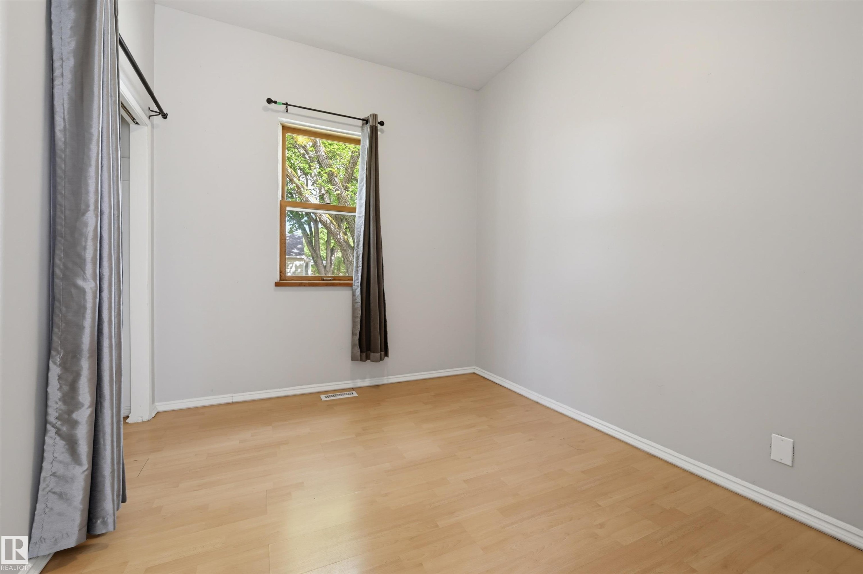 Bright interior space featuring wood-finish flooring, light grey painted walls, white baseboards, and a double-hung window with wood trim - 11450 71 Street Nw, Edmonton, AB
