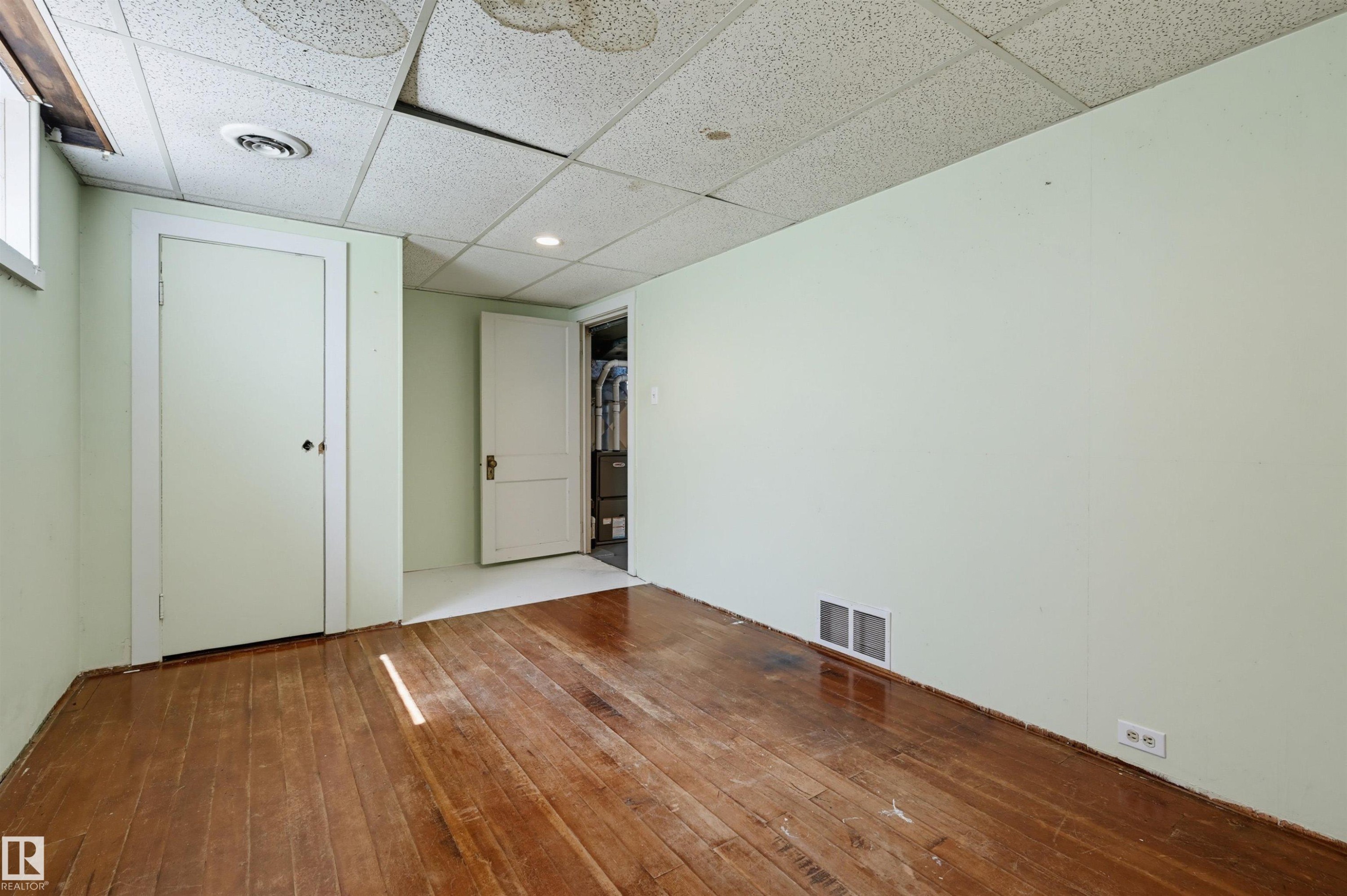 Room featuring wood flooring, light green walls, a white paneled door, and a drop ceiling - 11450 71 Street Nw, Edmonton, AB