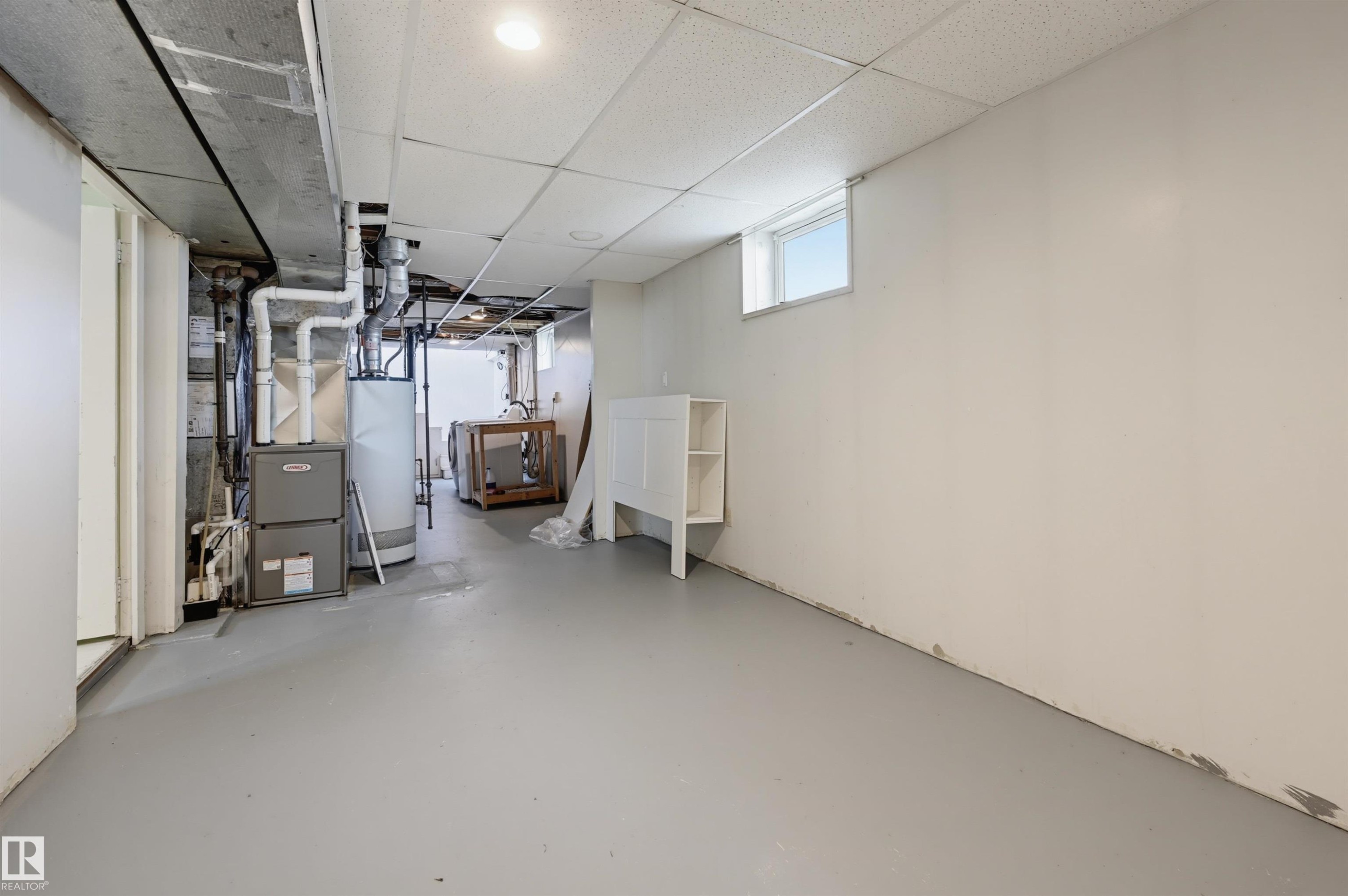 Unfinished basement area featuring a utility furnace and water heater, exposed ductwork, a drop ceiling, and a high-set window - 11450 71 Street Nw, Edmonton, AB