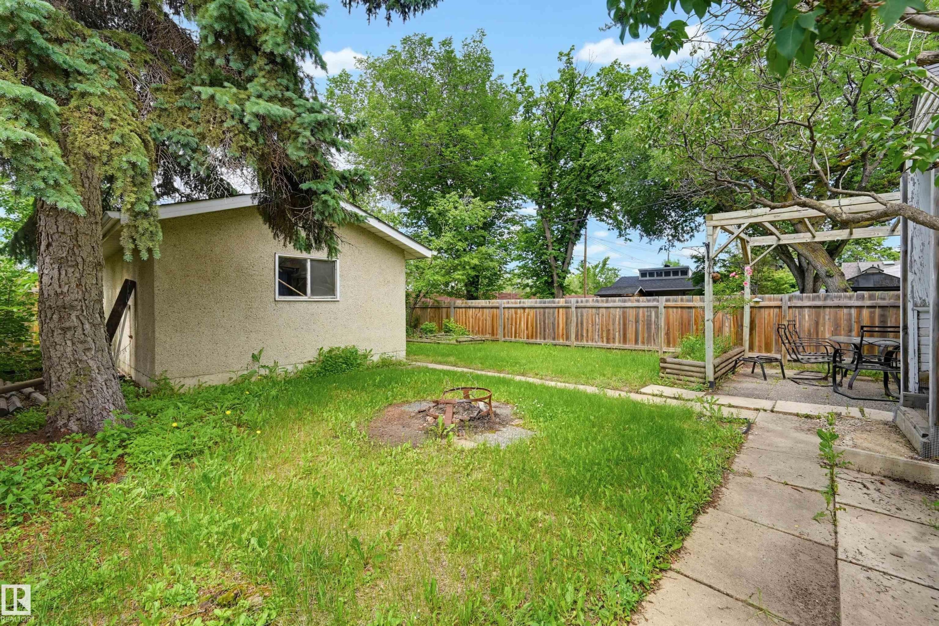 Expansive backyard featuring a detached storage shed, privacy fencing, mature trees, and a paved patio with a pergola structure - 11450 71 Street Nw, Edmonton, AB