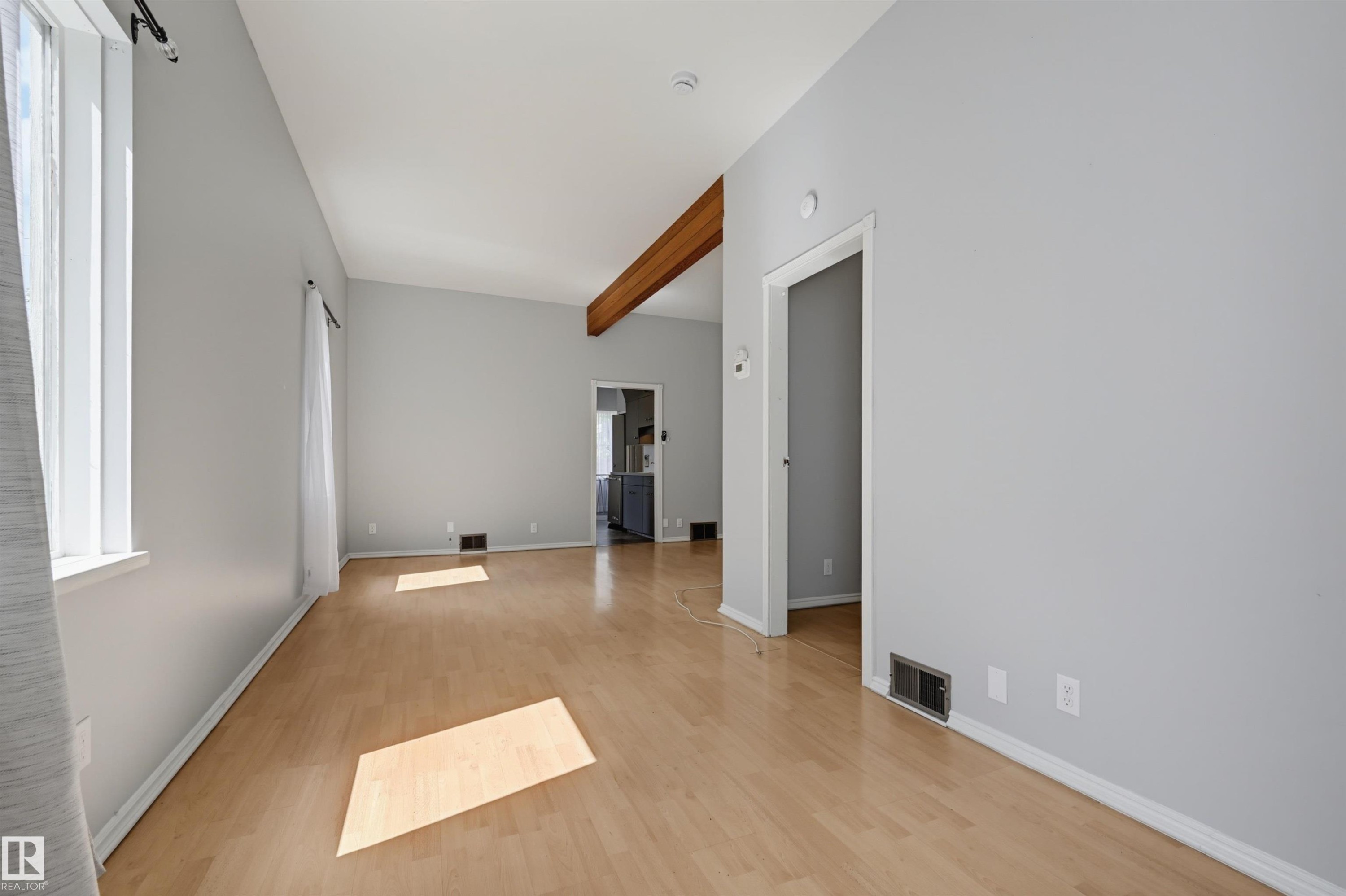 Spacious room featuring wood-finish flooring, light grey walls, and a vaulted ceiling with an exposed wood beam - 11450 71 Street Nw, Edmonton, AB