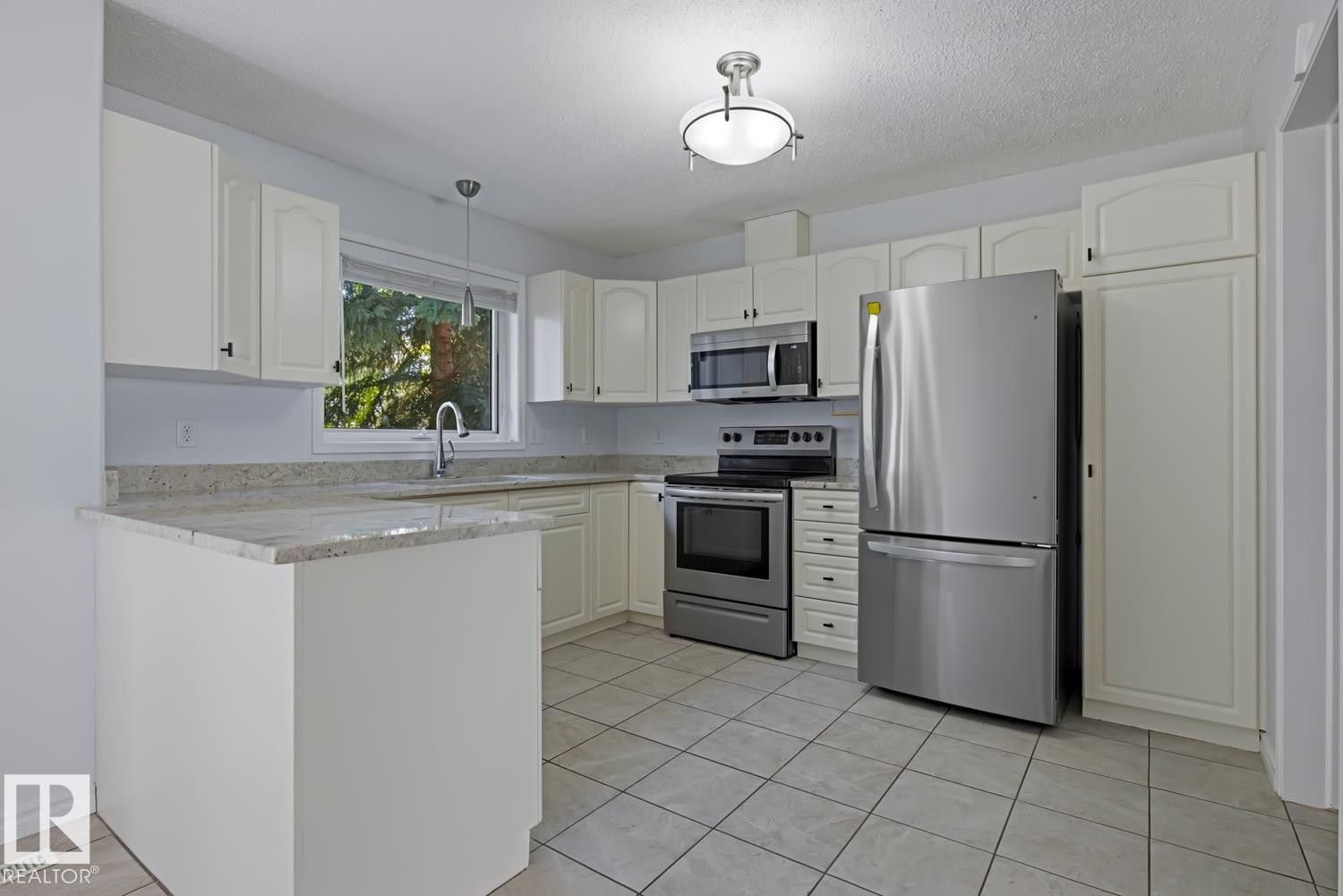 Contemporary kitchen featuring white cabinetry, light-toned countertops, stainless steel appliances, and tiled flooring - 6 1237 Carter Crest Road, Edmonton, AB