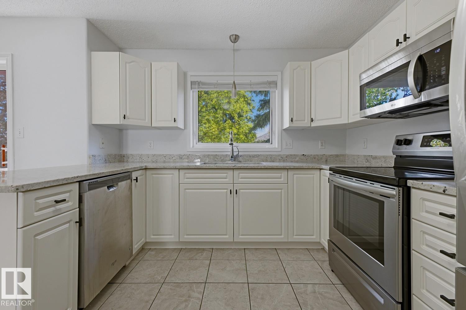 Kitchen featuring white cabinetry, light-toned countertops, a stainless steel dishwasher, a stainless steel range with an overhead microwave, and neutral-toned tiled flooring - 6 1237 Carter Crest Road, Edmonton, AB