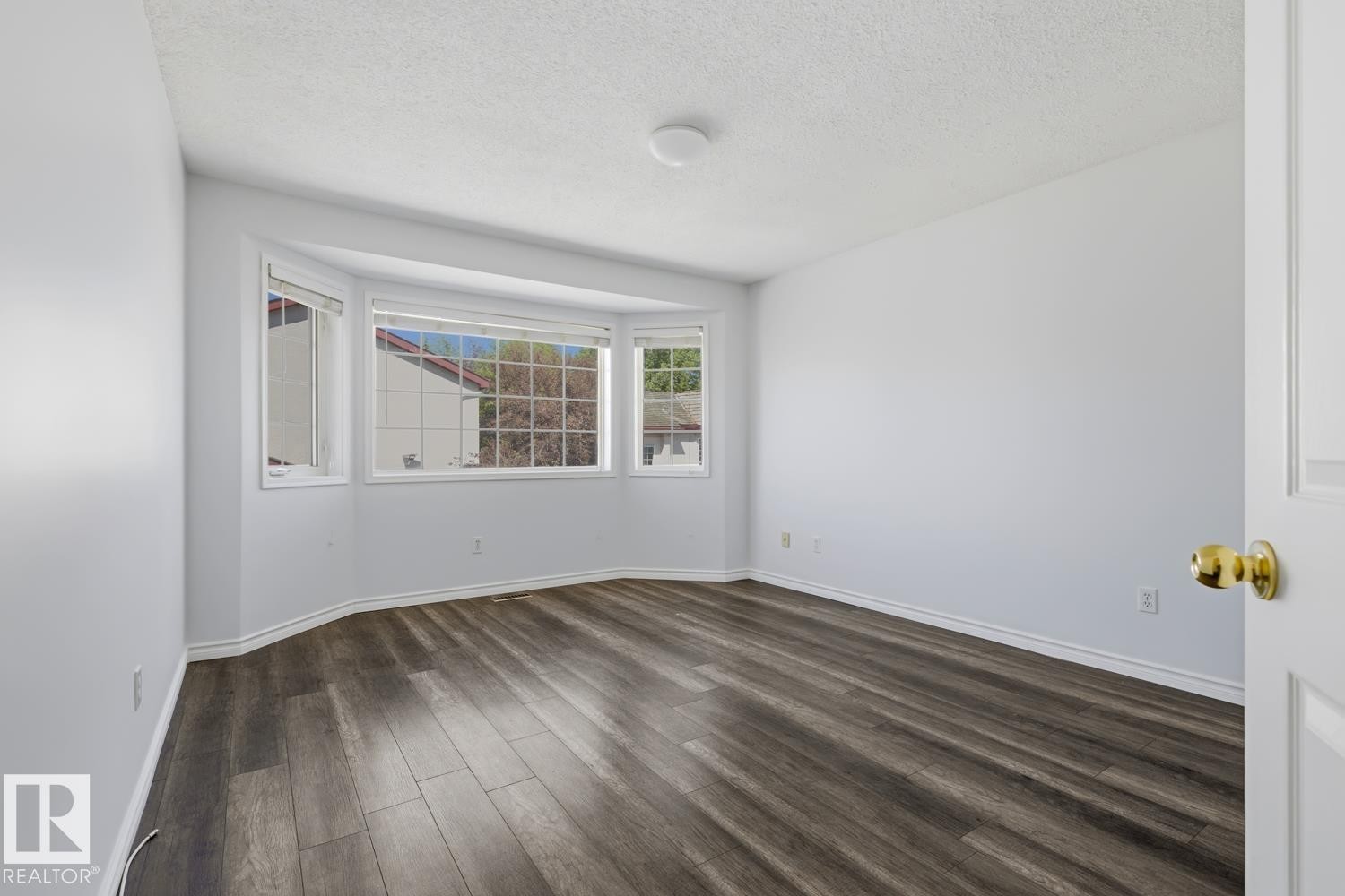 Spacious room featuring a bay window, wood-finish flooring, white baseboards, and a neutral wall color - 6 1237 Carter Crest Road, Edmonton, AB