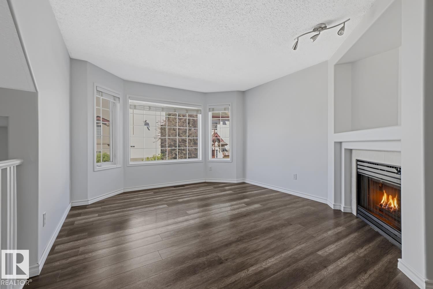 Living space featuring a corner fireplace with a white mantel, bay windows, and dark wood-finish flooring - 6 1237 Carter Crest Road, Edmonton, AB
