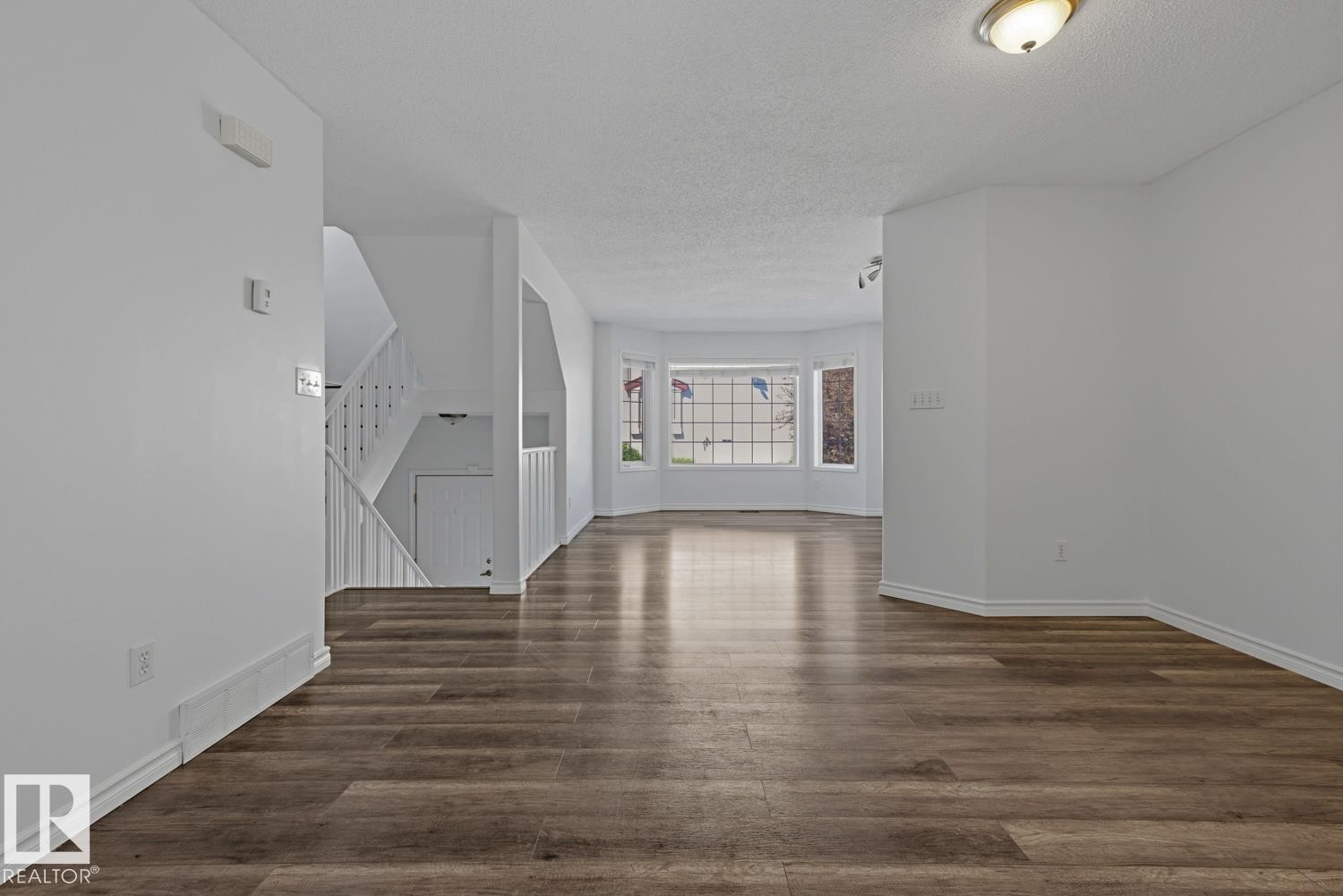 Spacious interior featuring wood-finish flooring throughout, a multi-pane bay window, and a white baluster staircase - 6 1237 Carter Crest Road, Edmonton, AB