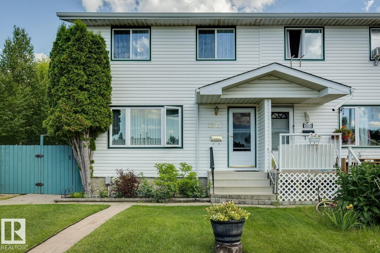 Duplex exterior featuring white siding with dark trim, a covered porch entry, and a manicured front lawn - 3015 131 Avenue, Edmonton, AB
