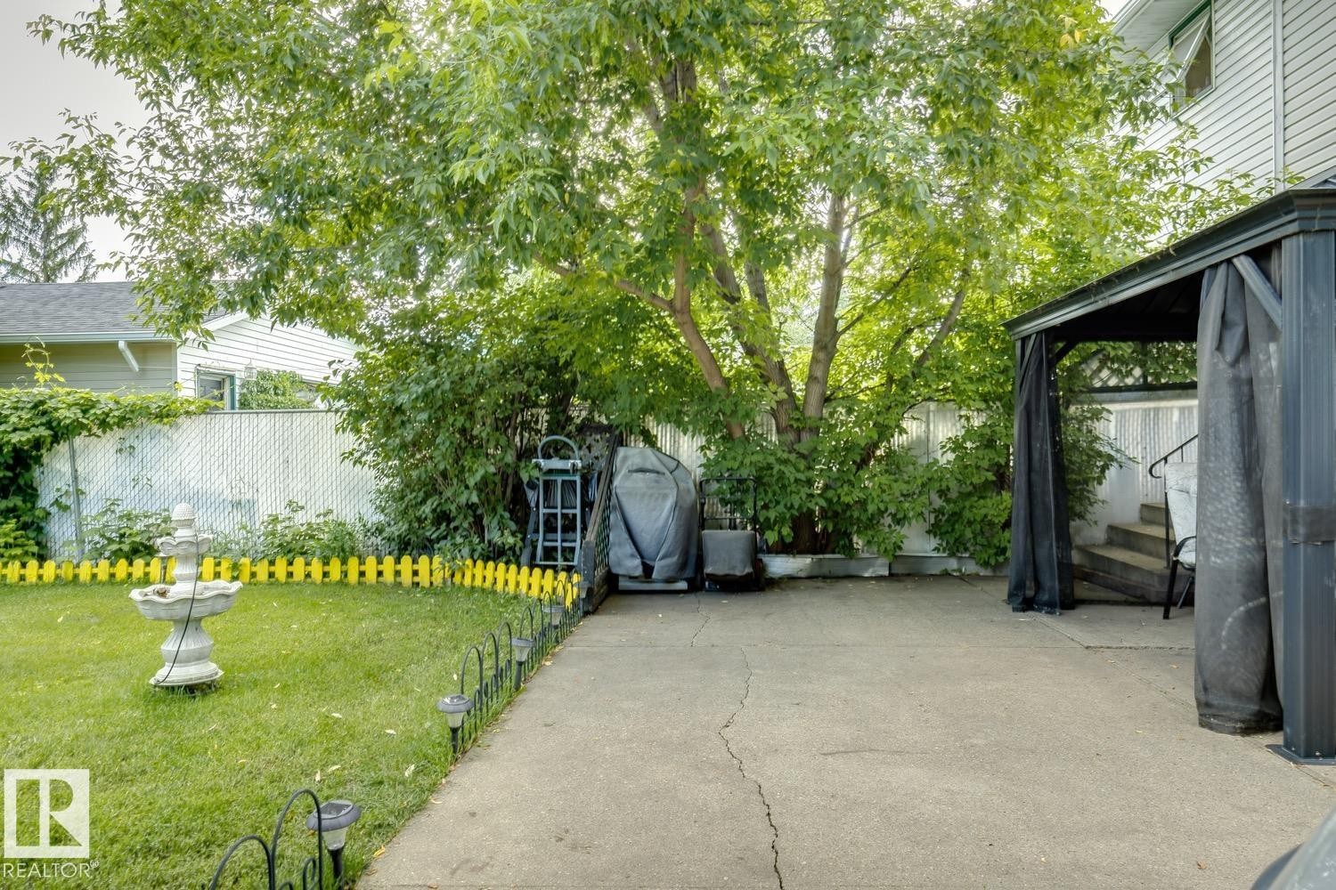 Landscaped backyard featuring a concrete patio, mature tree, and a covered gazebo structure - 3015 131 Avenue, Edmonton, AB