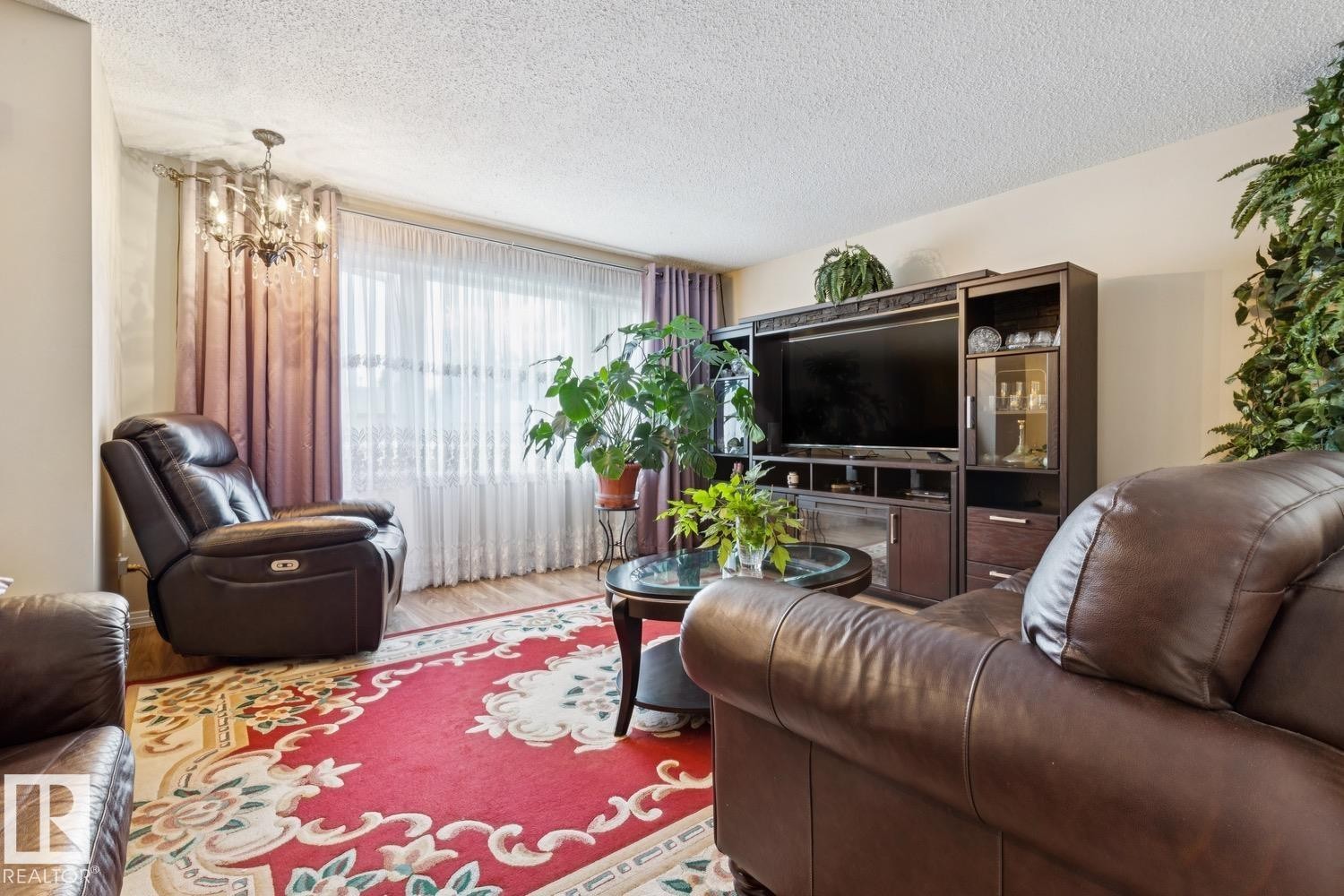 Living area featuring wood-finish flooring, a contemporary chandelier, and a built-in media console with display cabinetry - 3015 131 Avenue, Edmonton, AB