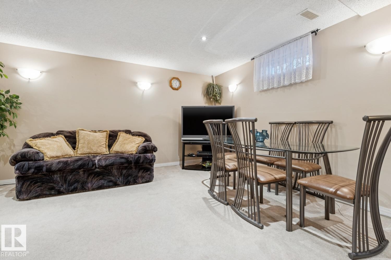 Carpeted room with neutral-toned walls, featuring a recessed ceiling light, wall-mounted sconces, and a high window with privacy covering - 3015 131 Avenue, Edmonton, AB