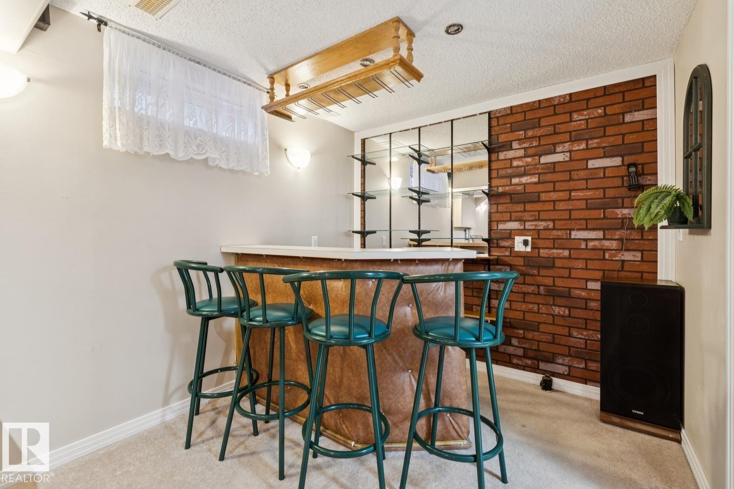 Dedicated bar area featuring a light-toned countertop, a suspended wooden glass rack, and integrated shelving with mirrored backing - 3015 131 Avenue, Edmonton, AB