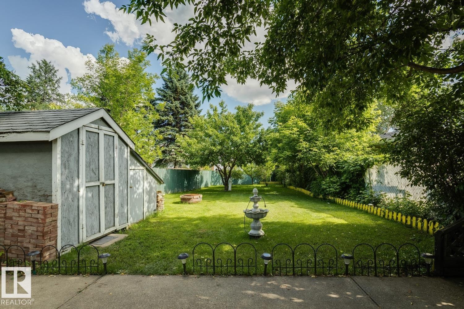 Expansive backyard featuring a lush lawn, mature trees, and a detached storage shed with a shingled roof - 3015 131 Avenue, Edmonton, AB