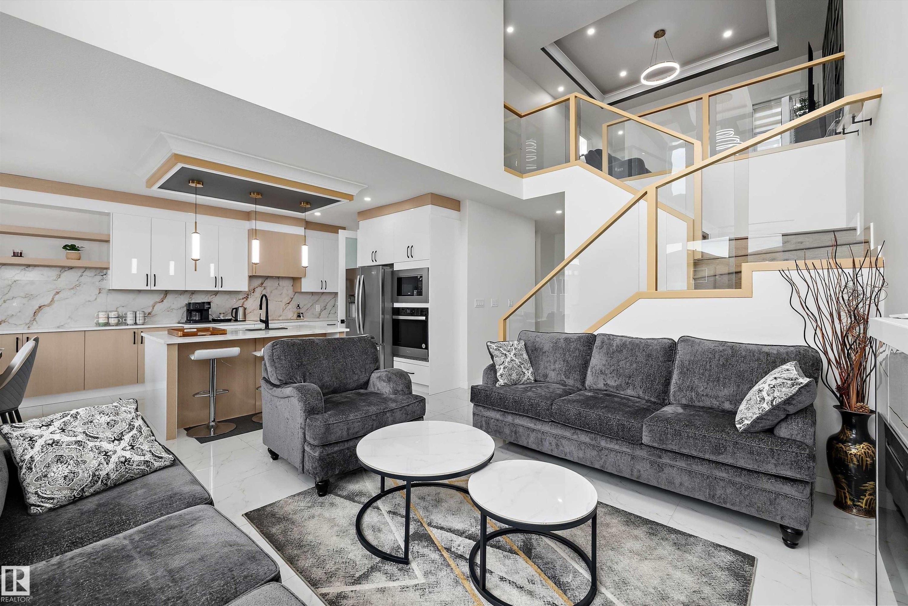 Open-concept living space featuring a two-story ceiling, a modern kitchen with a waterfall island, integrated stainless steel appliances, and a contemporary glass and wood-finish staircase - 403 Pine Point, Leduc, AB