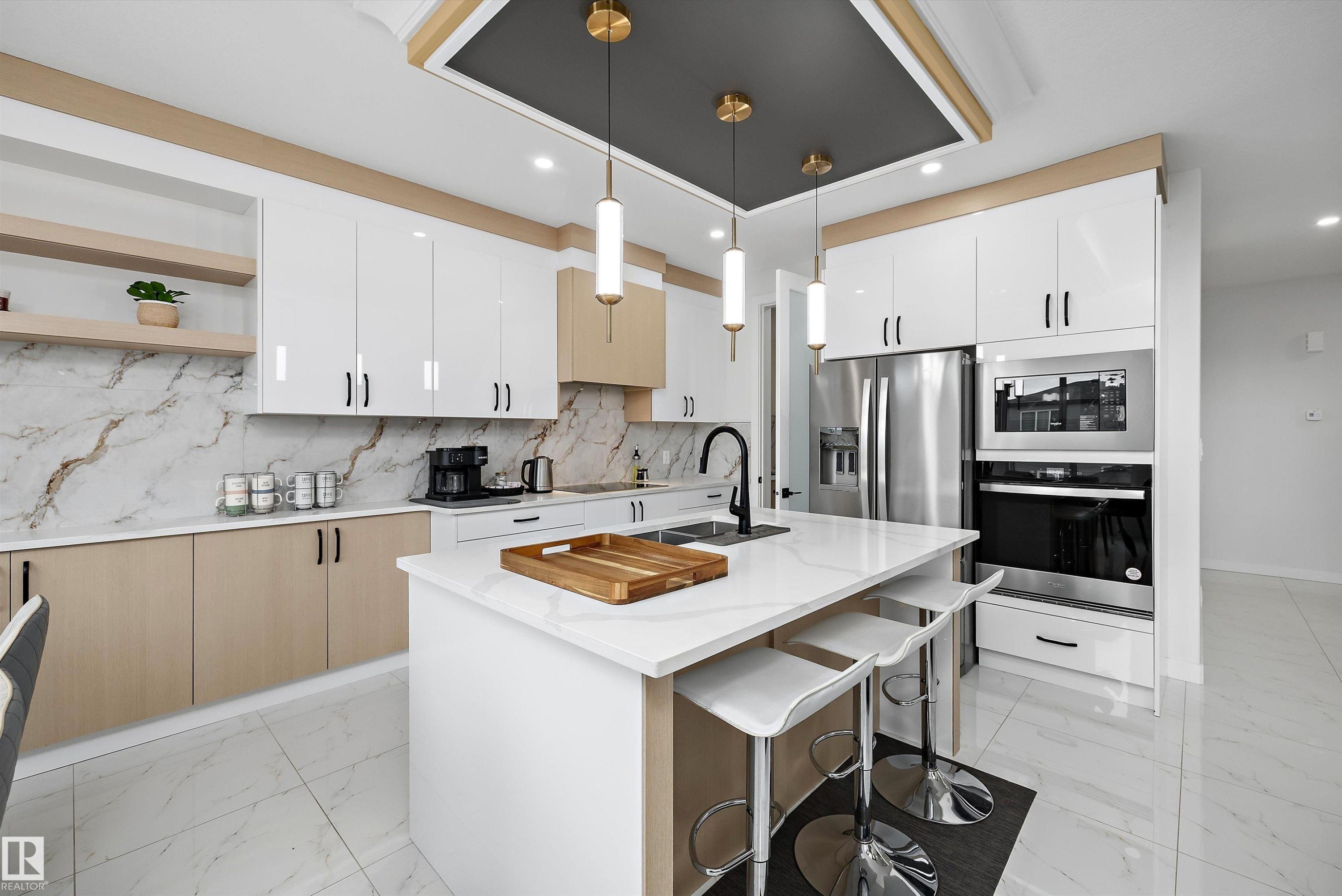 Contemporary kitchen featuring a central island with a white countertop, two-tone cabinetry, integrated stainless steel appliances, a complementary backsplash, and pendant lighting - 403 Pine Point, Leduc, AB
