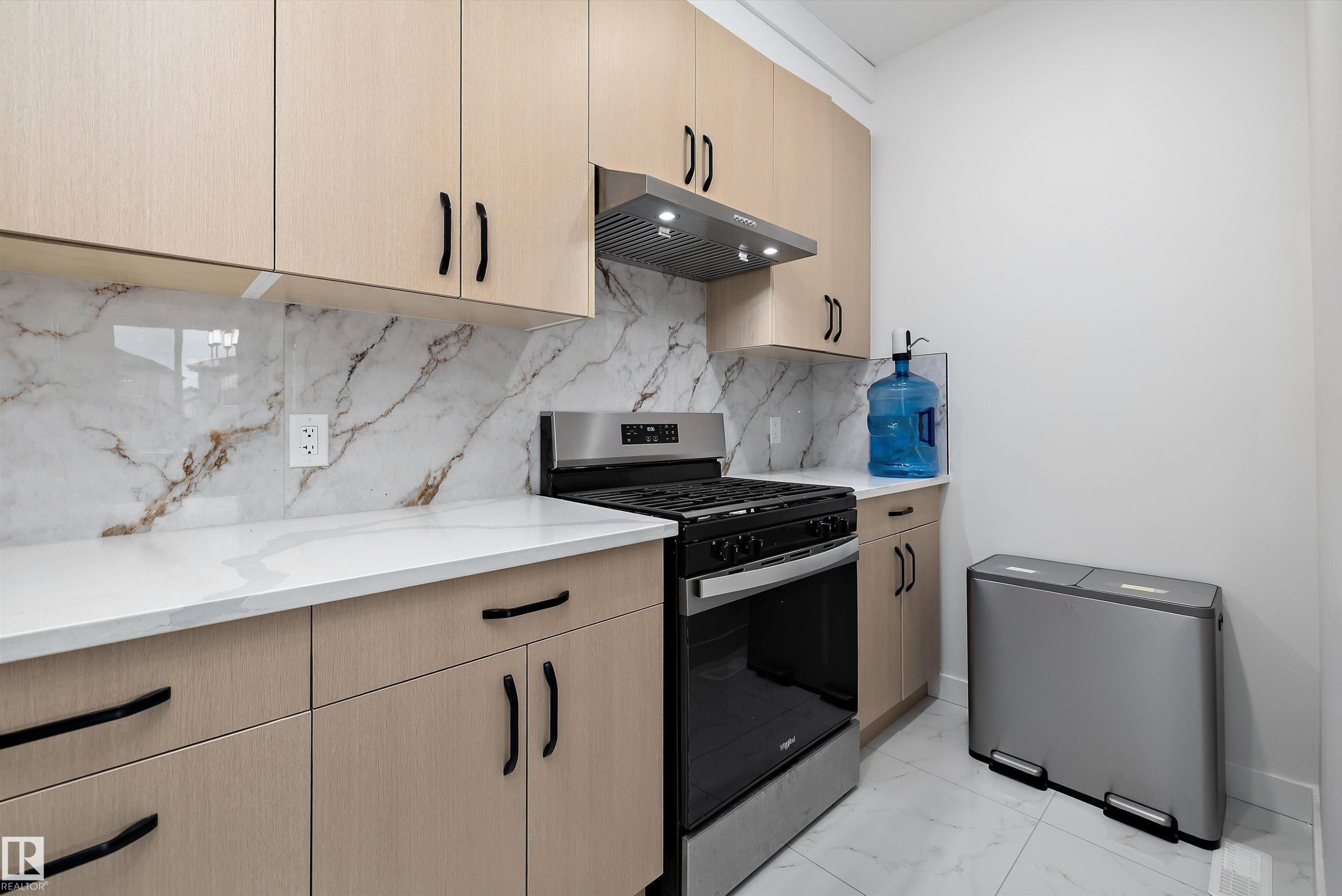 Kitchen featuring light wood-finish cabinetry with black hardware, white countertops, and a white and brown veined backsplash - 403 Pine Point, Leduc, AB