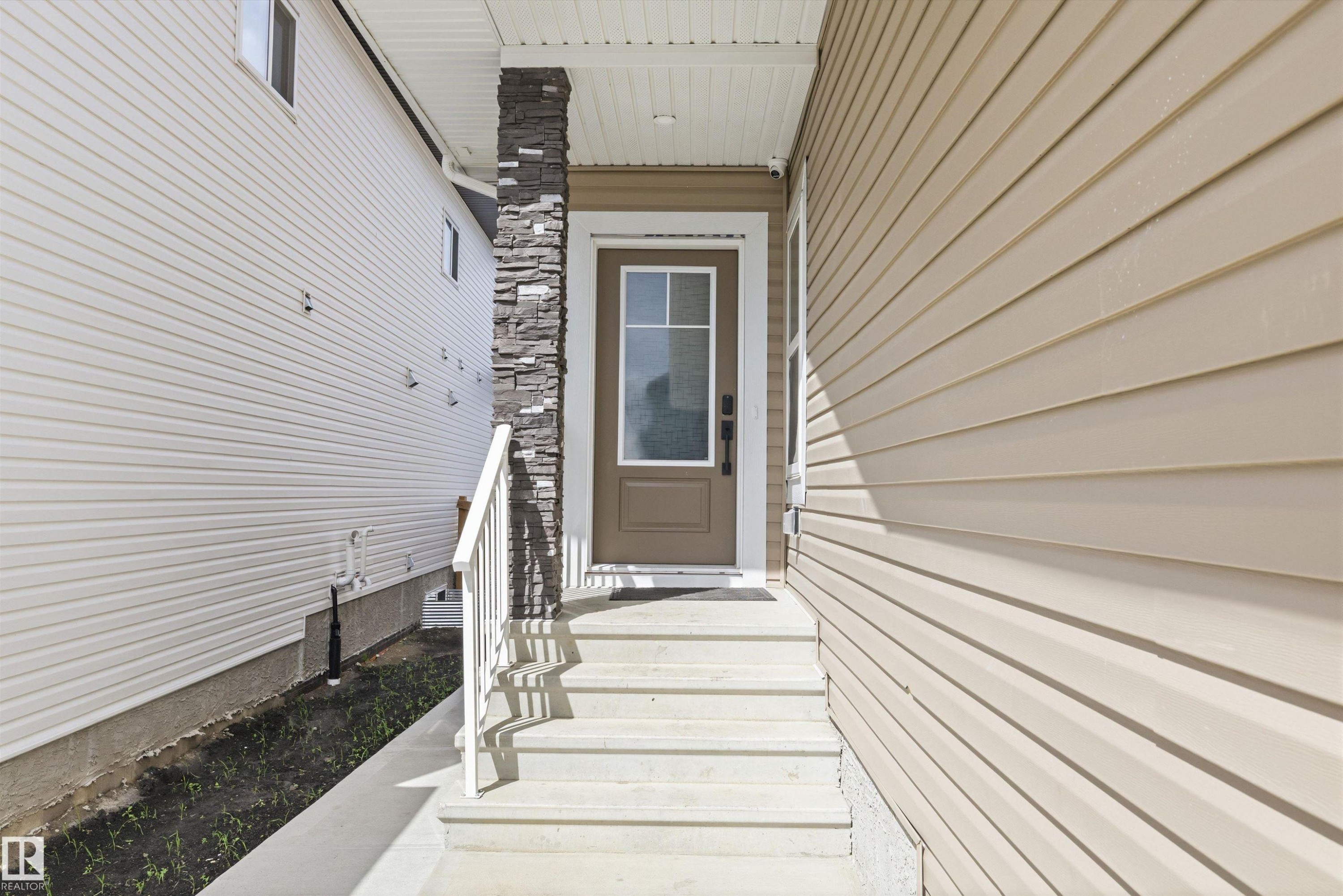 Front entrance featuring a brown door with clear glass panels, concrete steps, and a white handrail - 403 Pine Point, Leduc, AB