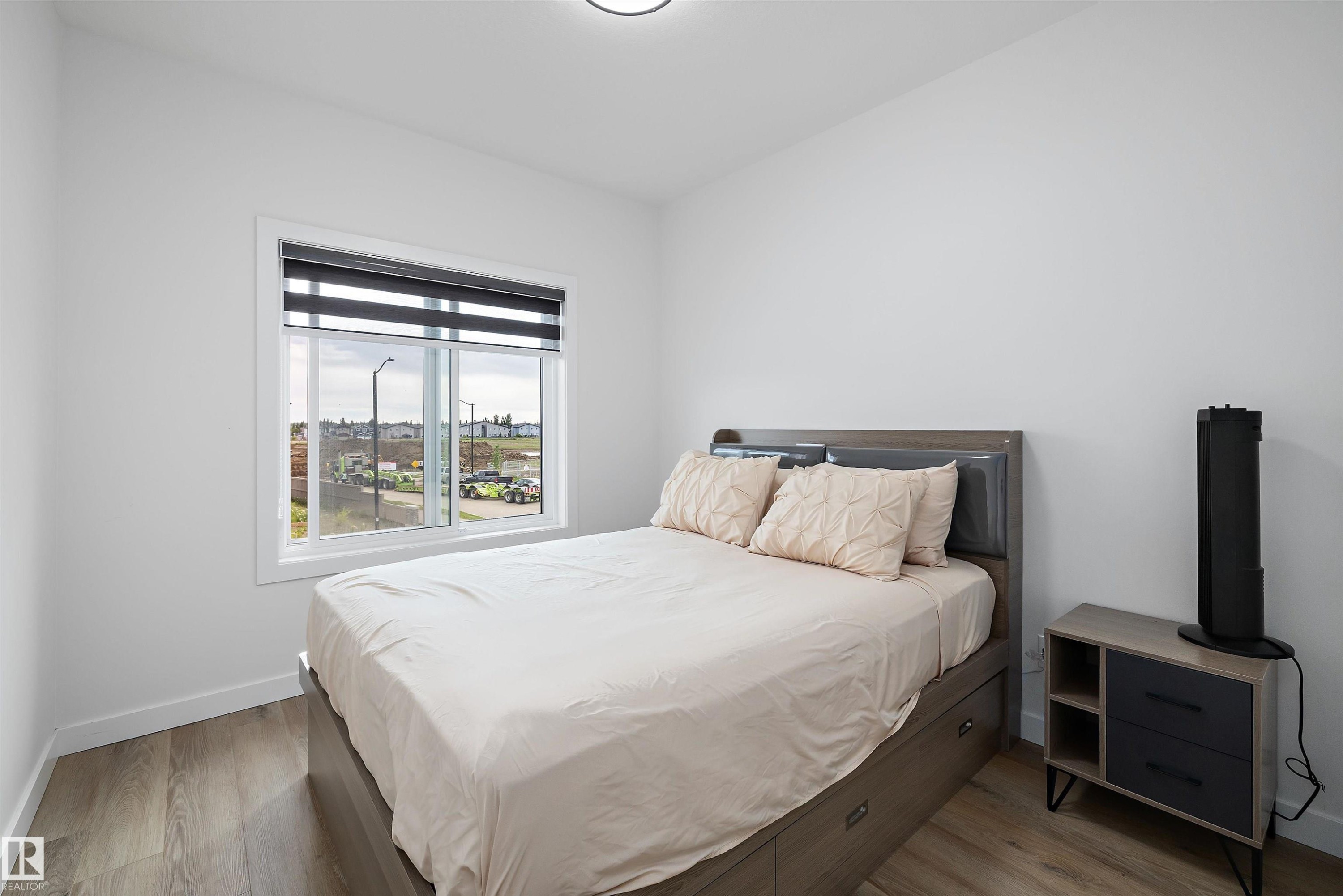 Bedroom featuring light-toned walls, a single window with blinds, and wood-finish flooring - 403 Pine Point, Leduc, AB