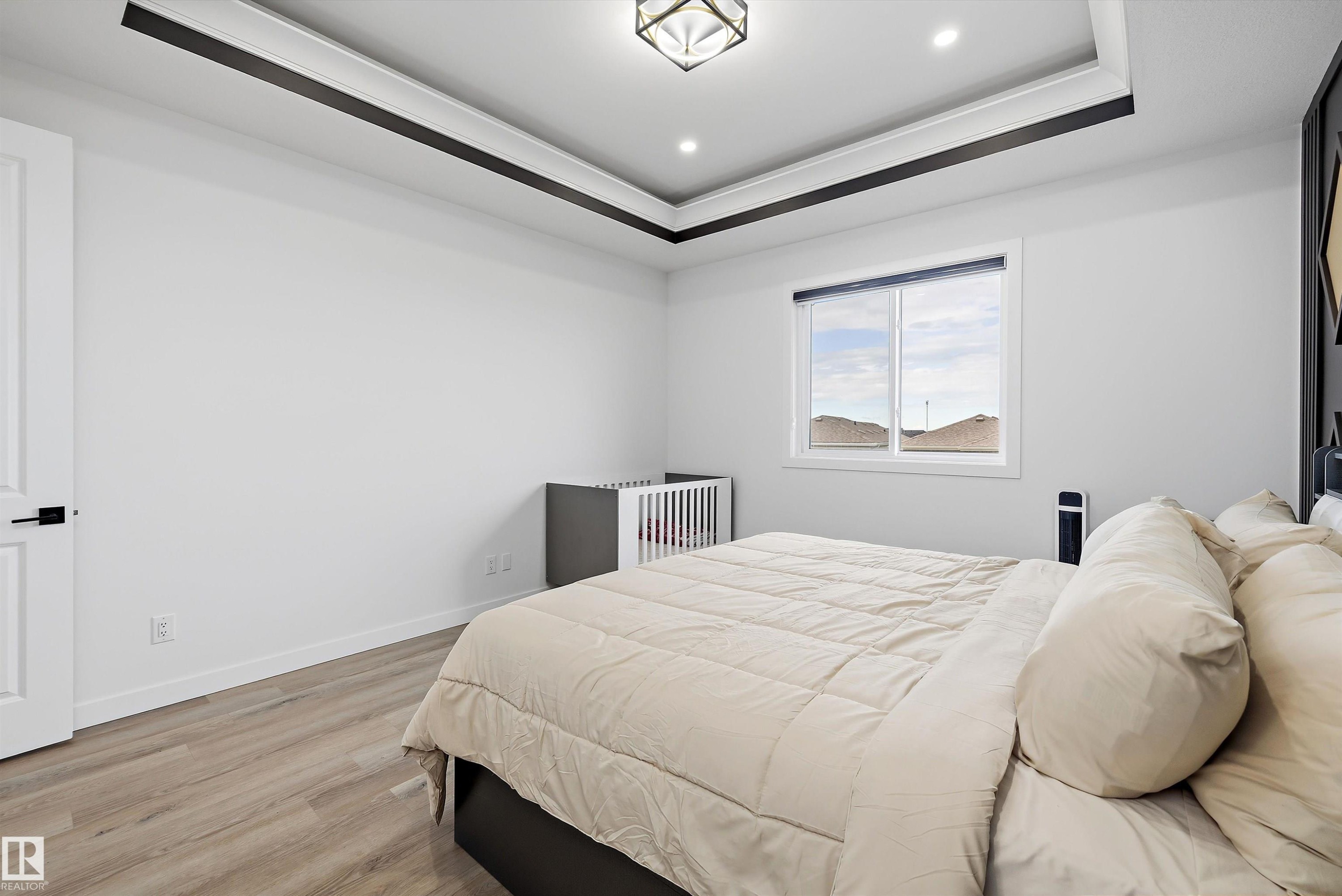 Recessed lighting illuminating a tray ceiling with dark accent trim, wood-finish flooring, and a single window - 403 Pine Point, Leduc, AB