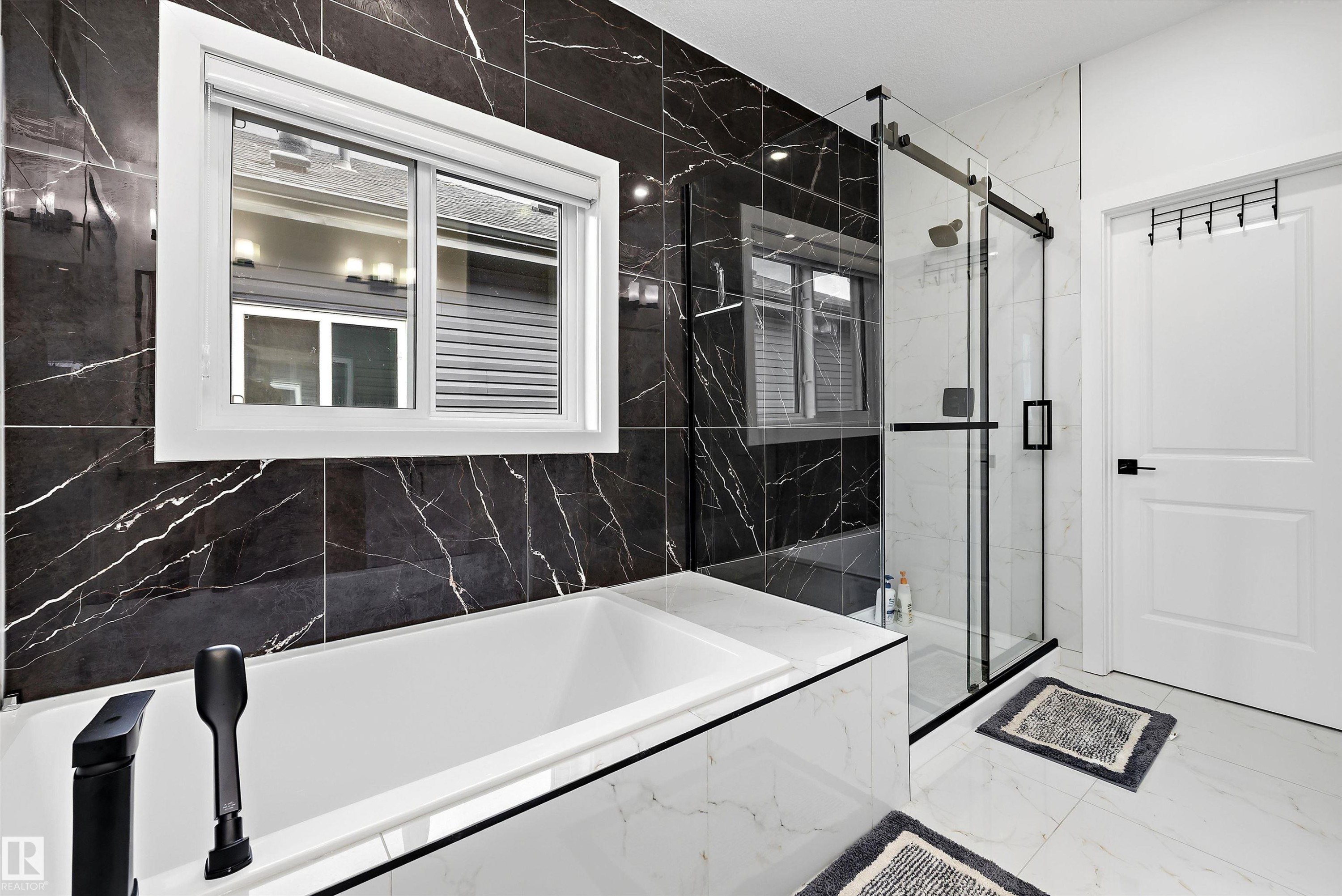 Contemporary bathroom featuring a built-in soaking tub with matte black fixtures, a spacious glass-enclosed shower with a sliding door, and a striking black and white marble-look tile surround - 403 Pine Point, Leduc, AB