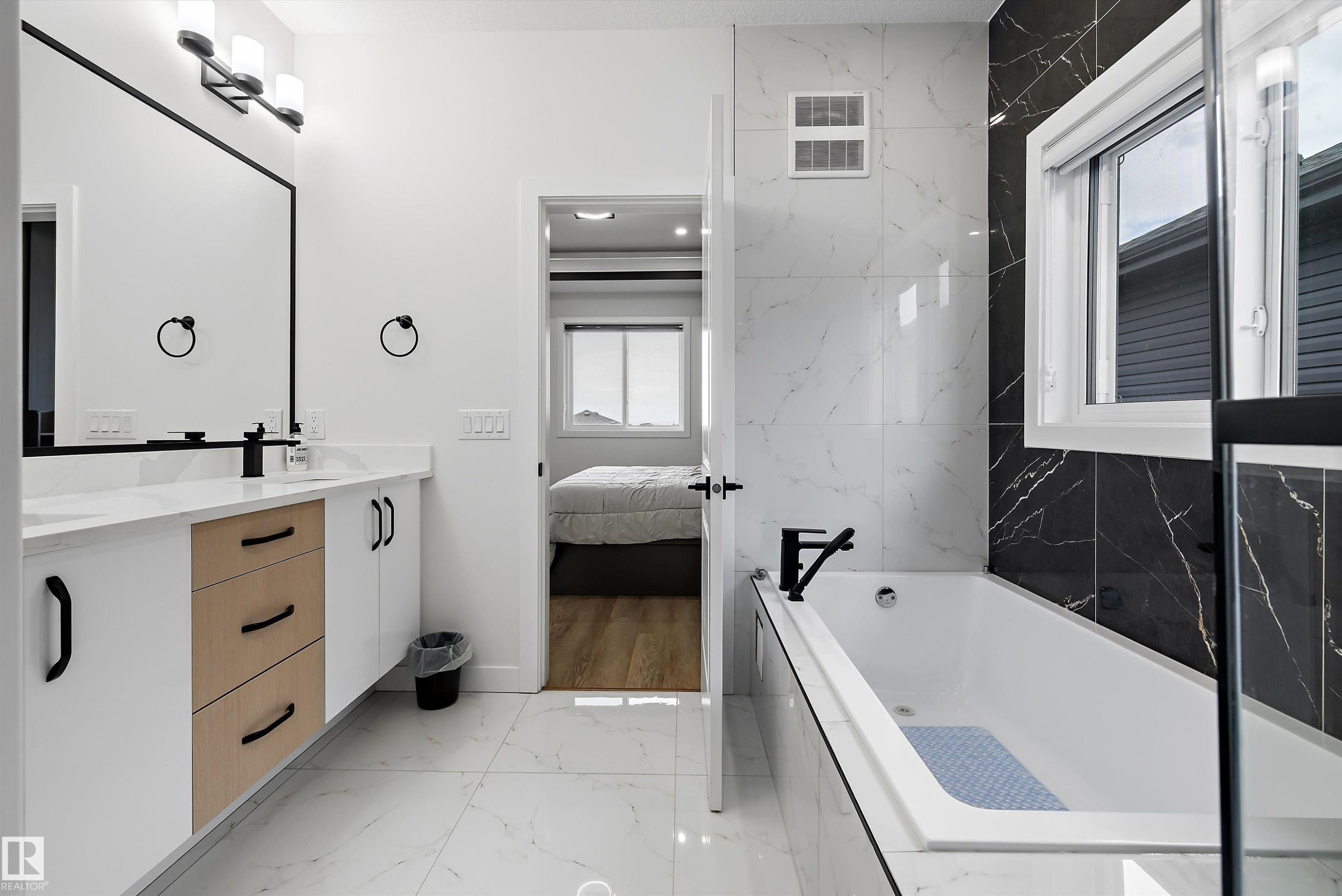 Contemporary bathroom featuring a combined shower and bathtub with matte black fixtures, white marble-look tile flooring, and a vanity with white cabinetry, wood-finish drawers, and a white countertop - 403 Pine Point, Leduc, AB