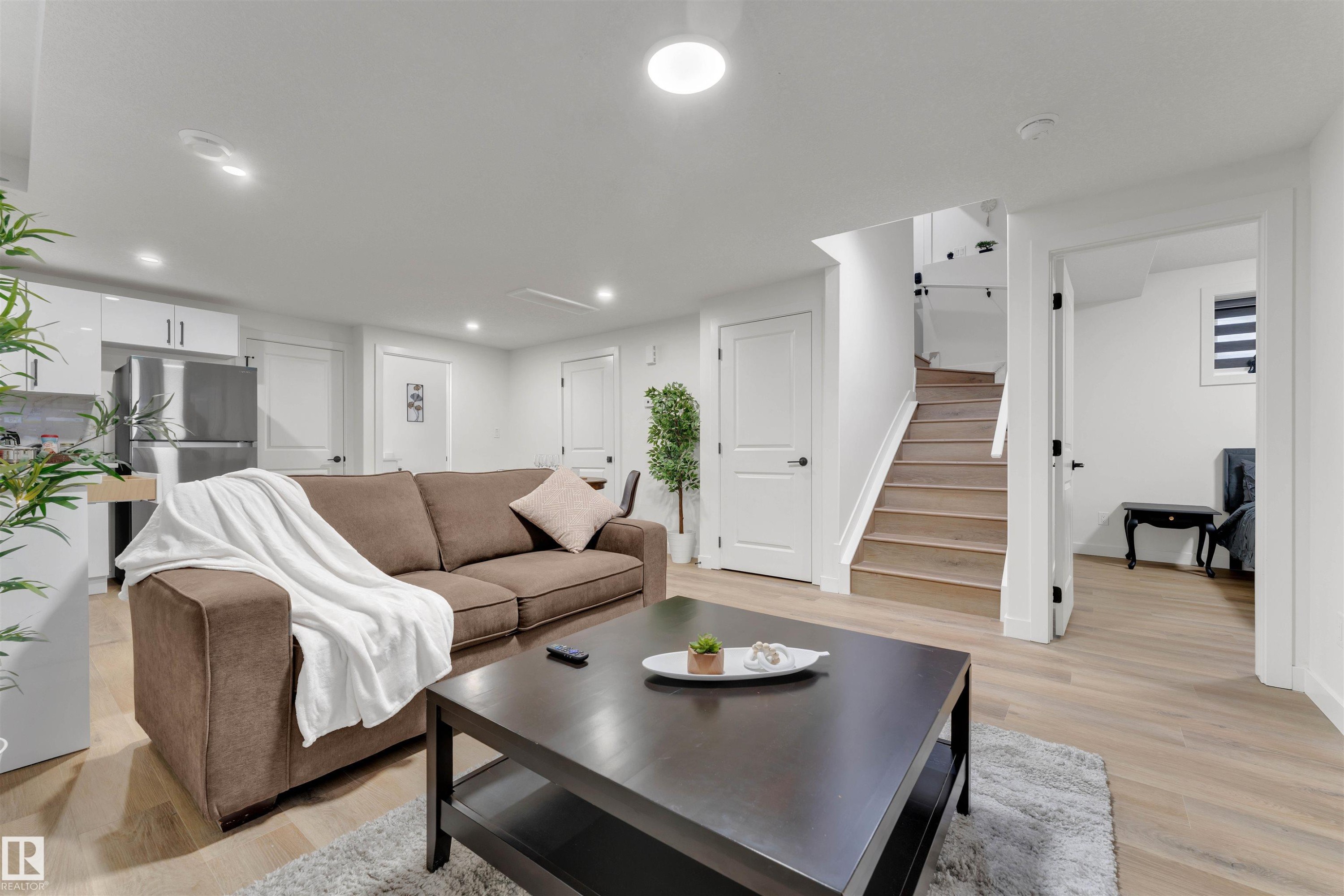 Open-concept living space featuring wood-finish flooring, recessed lighting, and a modern kitchen area with stainless steel appliances - 403 Pine Point, Leduc, AB