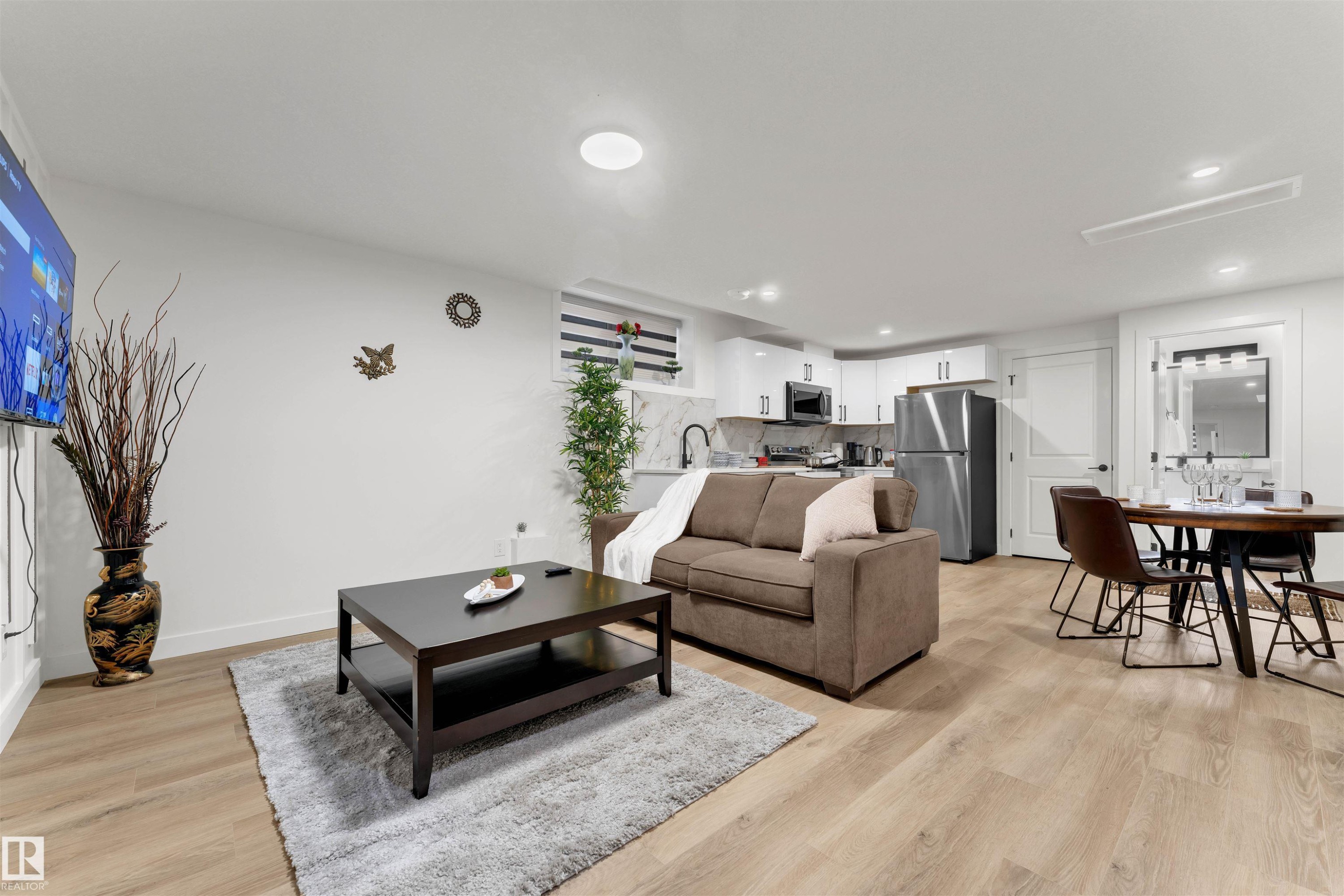 Open concept living space featuring wood-finish flooring, recessed lighting, and a modern kitchen with white cabinetry and stainless steel appliances - 403 Pine Point, Leduc, AB