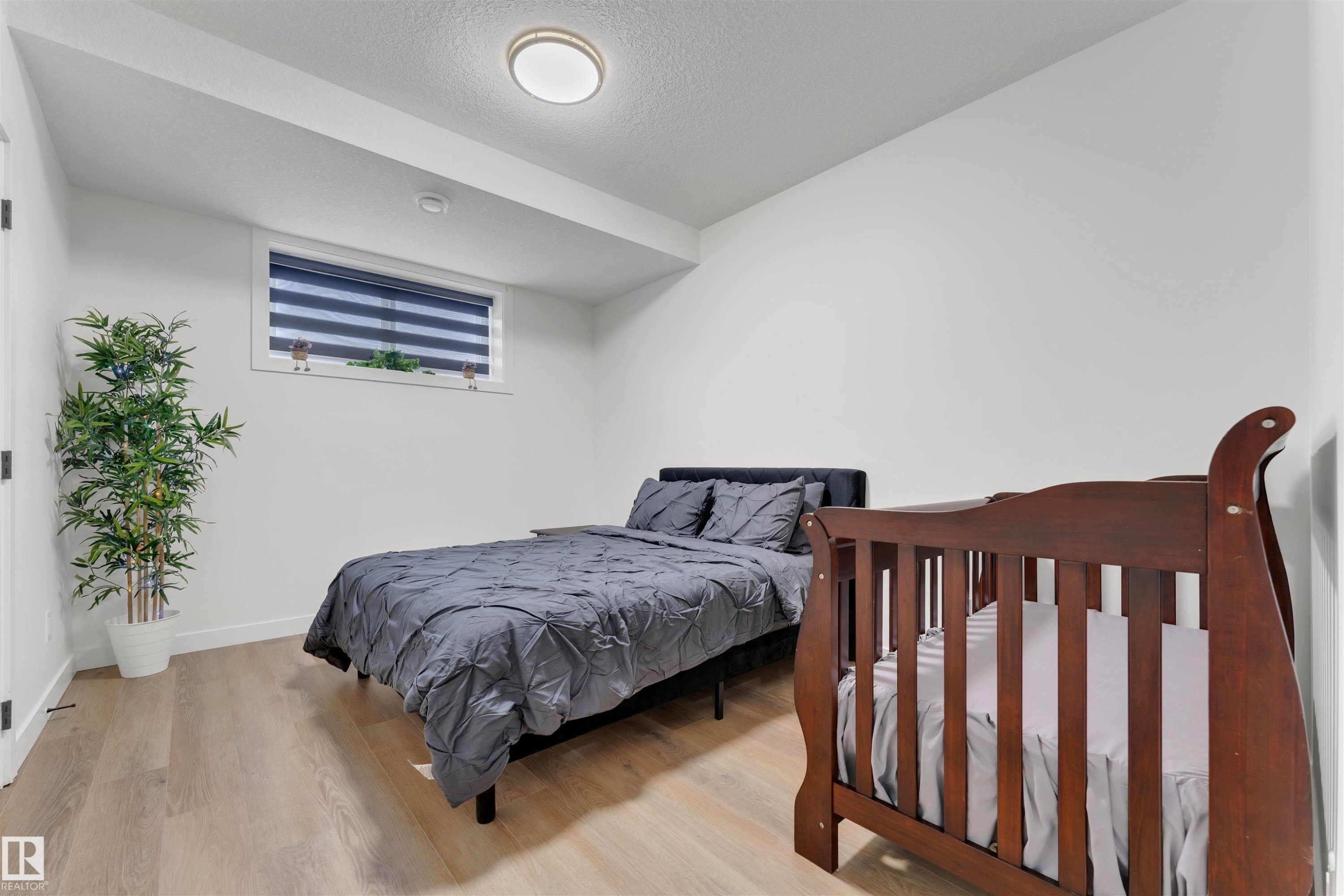 Spacious room featuring light wood-finish flooring, a contemporary flush-mount ceiling light, a transom window with horizontal blinds, and clean white walls - 403 Pine Point, Leduc, AB