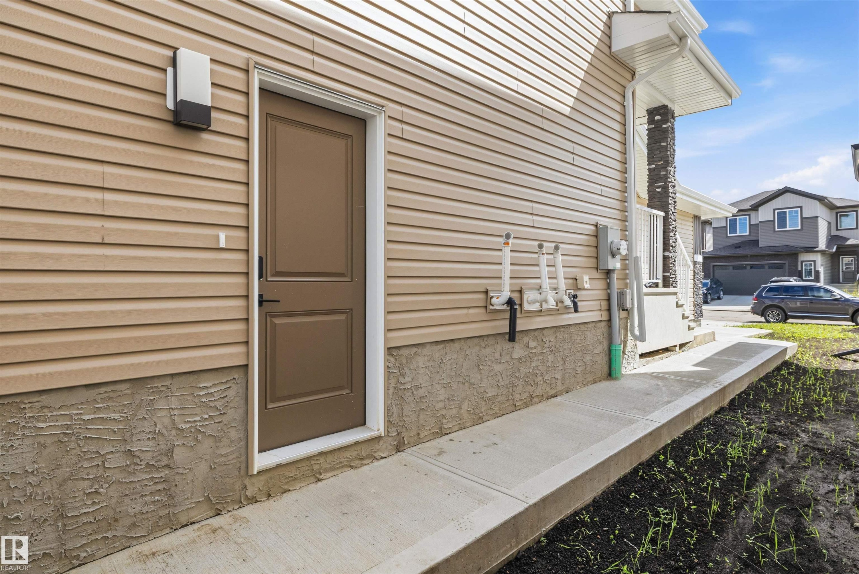 Exterior siding in a tan finish featuring a brown entry door with white trim, an exterior light fixture, and a concrete walkway - 403 Pine Point, Leduc, AB