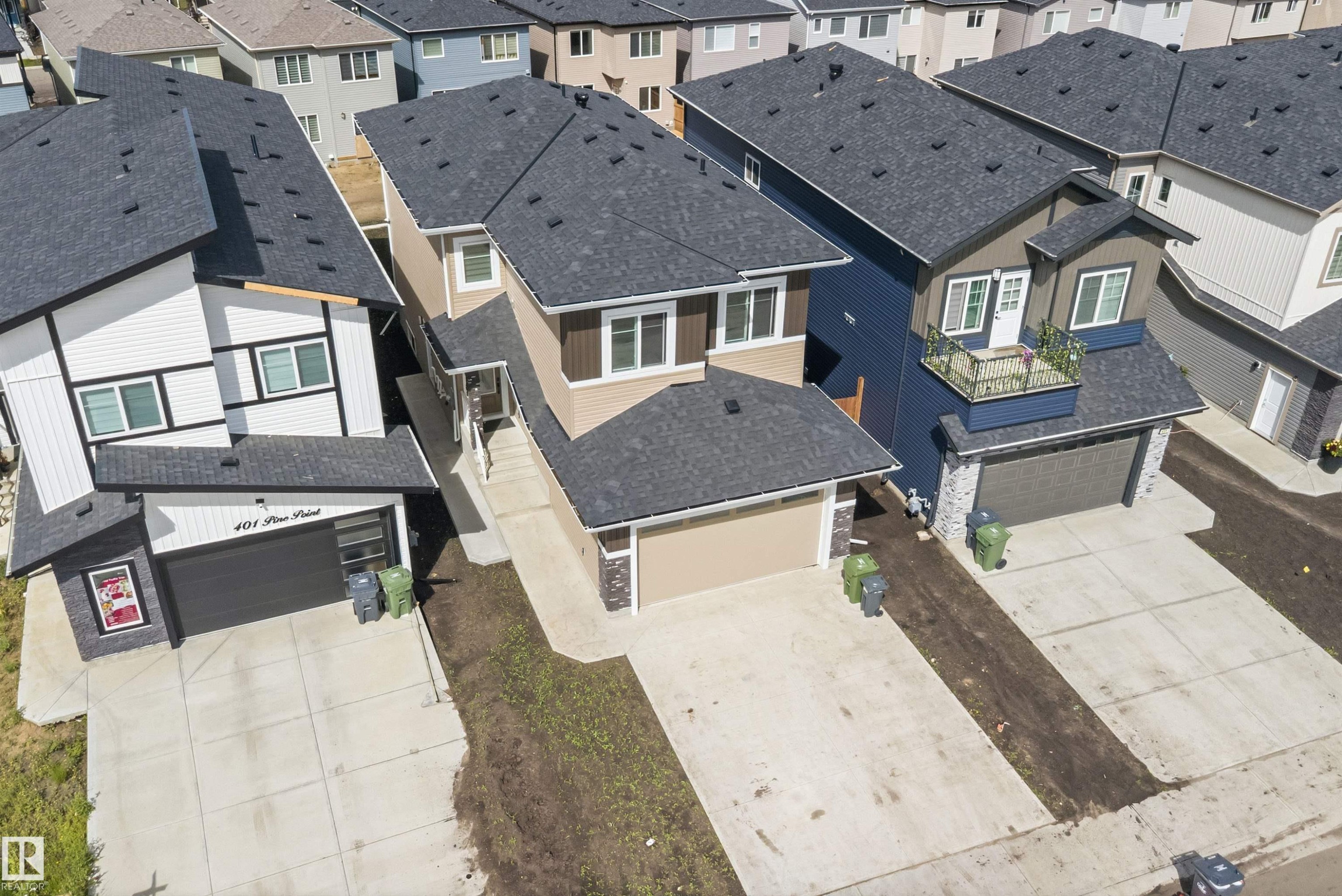 Modern two-story home featuring a dark shingle roof, attached garage with a dark door, light-colored siding, and white-framed windows - 403 Pine Point, Leduc, AB