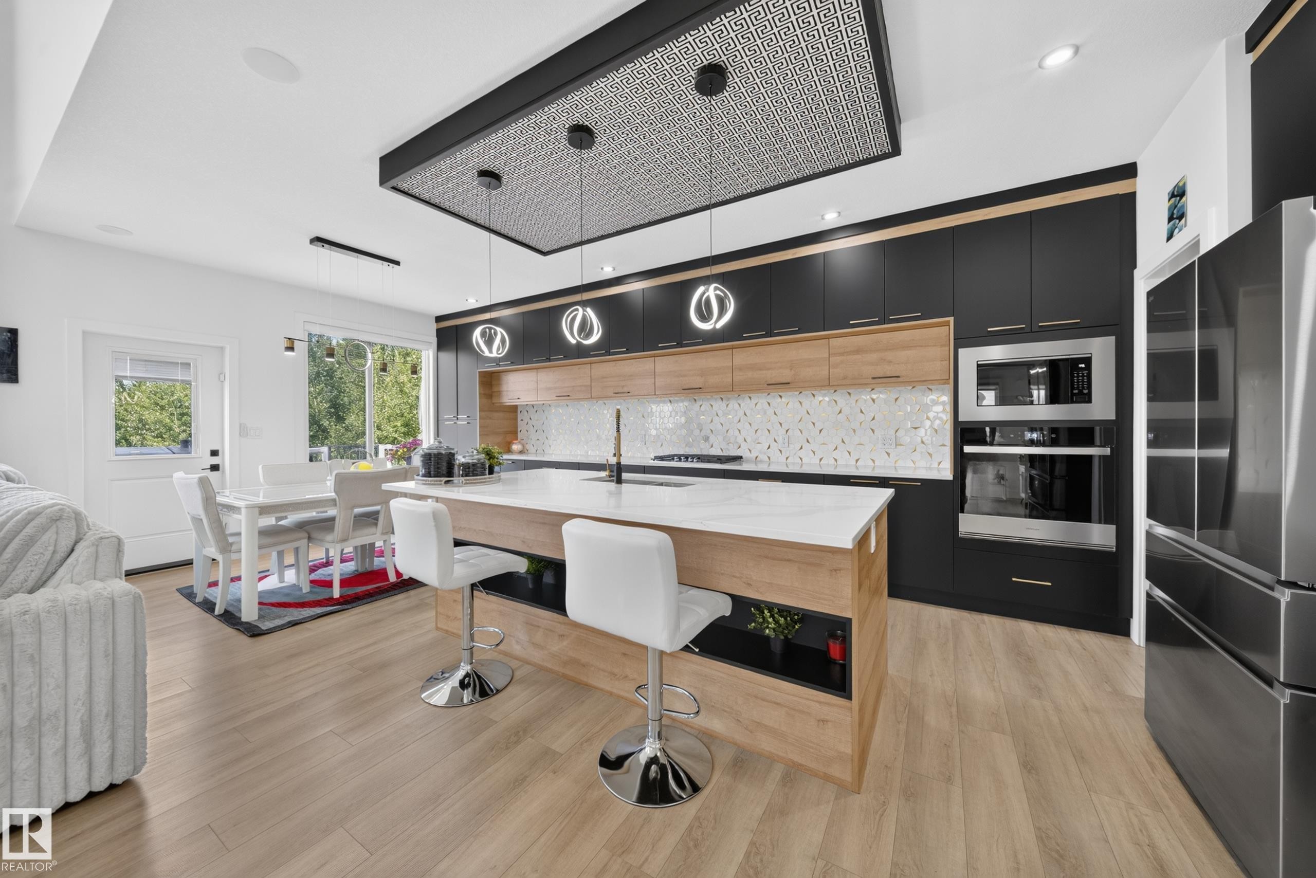 Contemporary kitchen featuring a large island with white countertop, rich dark cabinetry, light wood-finish accents, and stainless steel appliances - 626 Astoria Way, Devon, AB