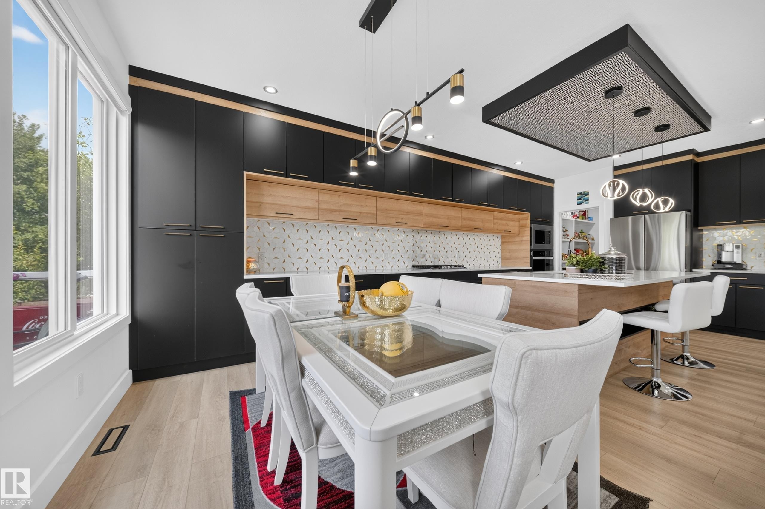 Modern kitchen featuring black and wood-finish cabinetry, an oversized island with seating, stainless steel appliances, and wood-finish flooring - 626 Astoria Way, Devon, AB