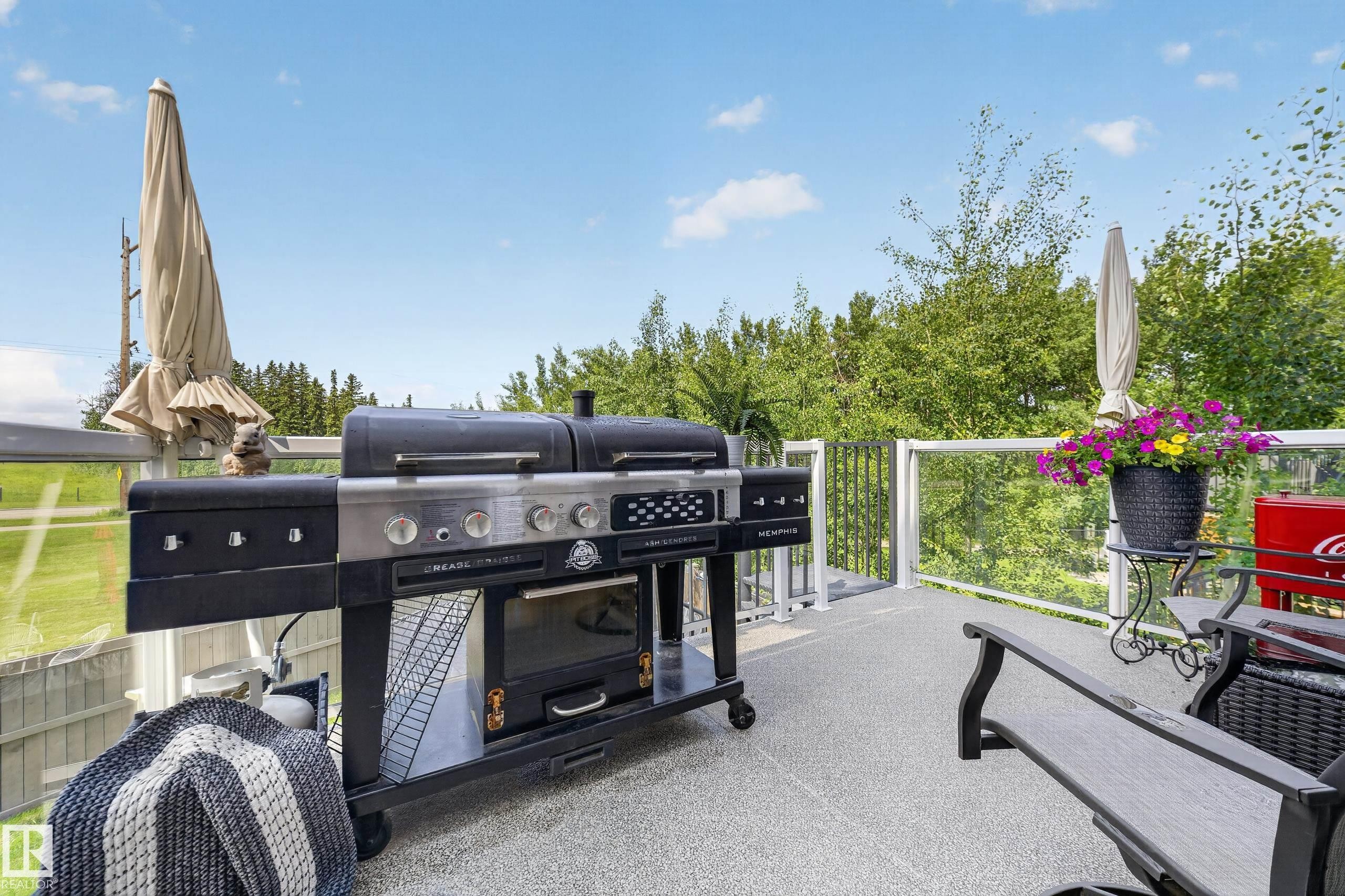 Expansive outdoor deck featuring a textured surface, clear glass railings, and multiple shade umbrellas - 626 Astoria Way, Devon, AB