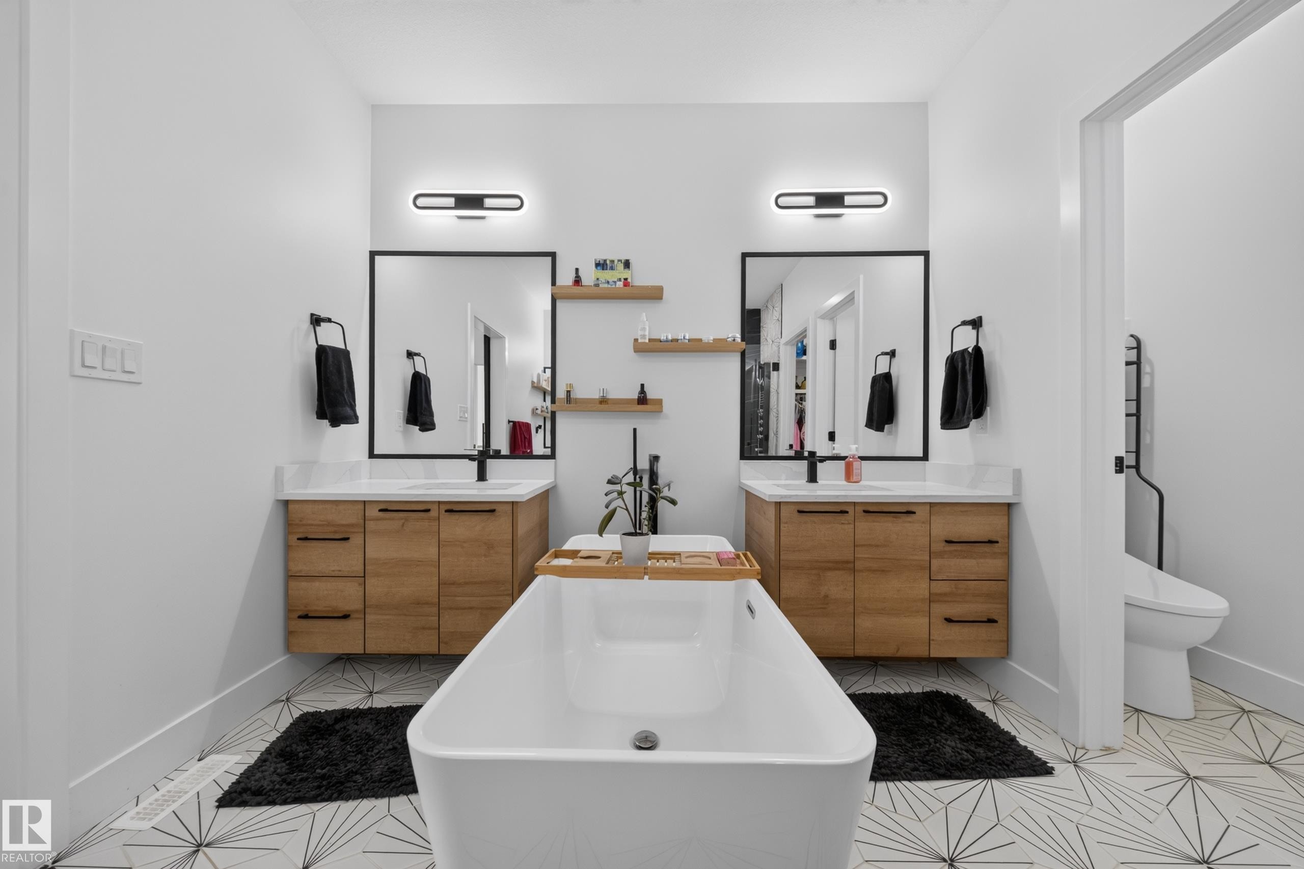 Contemporary bathroom featuring a freestanding soaking tub, dual floating wood-finish vanities with quartz countertops, and black-framed mirrors - 626 Astoria Way, Devon, AB