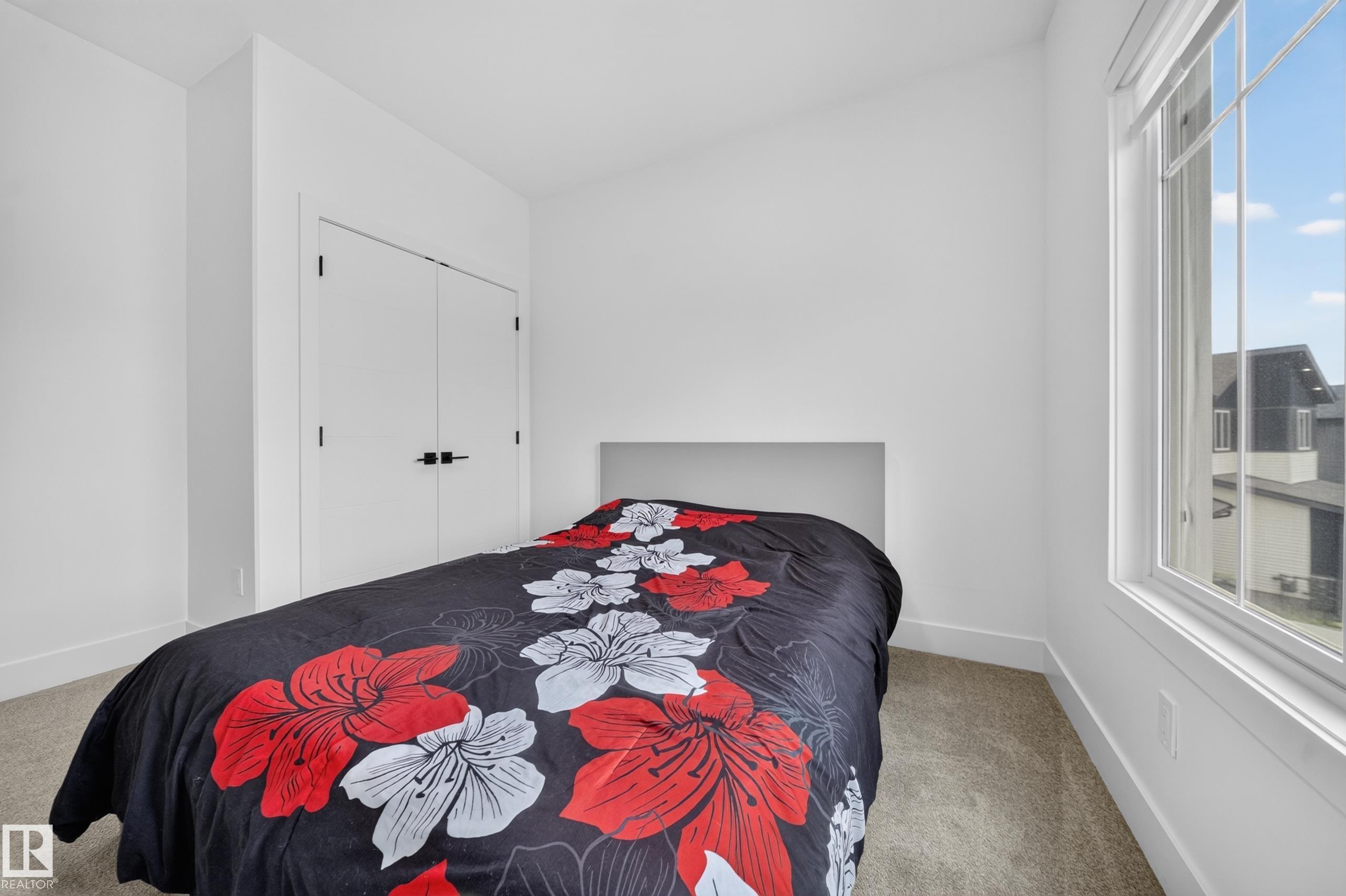 Bedroom featuring a large window, light-toned carpet flooring, white walls, and a closet with double doors and black hardware - 626 Astoria Way, Devon, AB